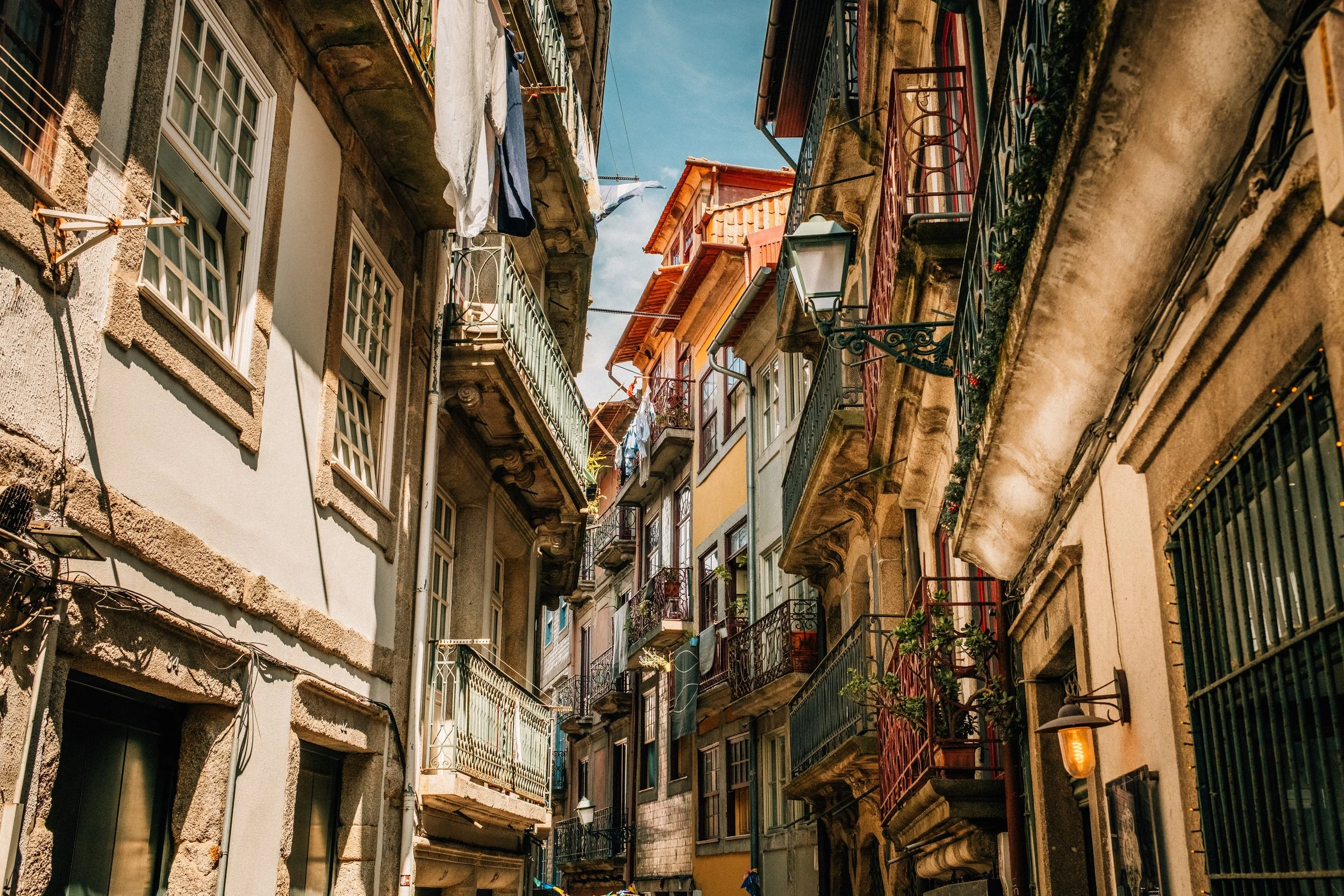 Tall, narrow apartment buildings with balconies and laundry hanging outside on a sunny day.