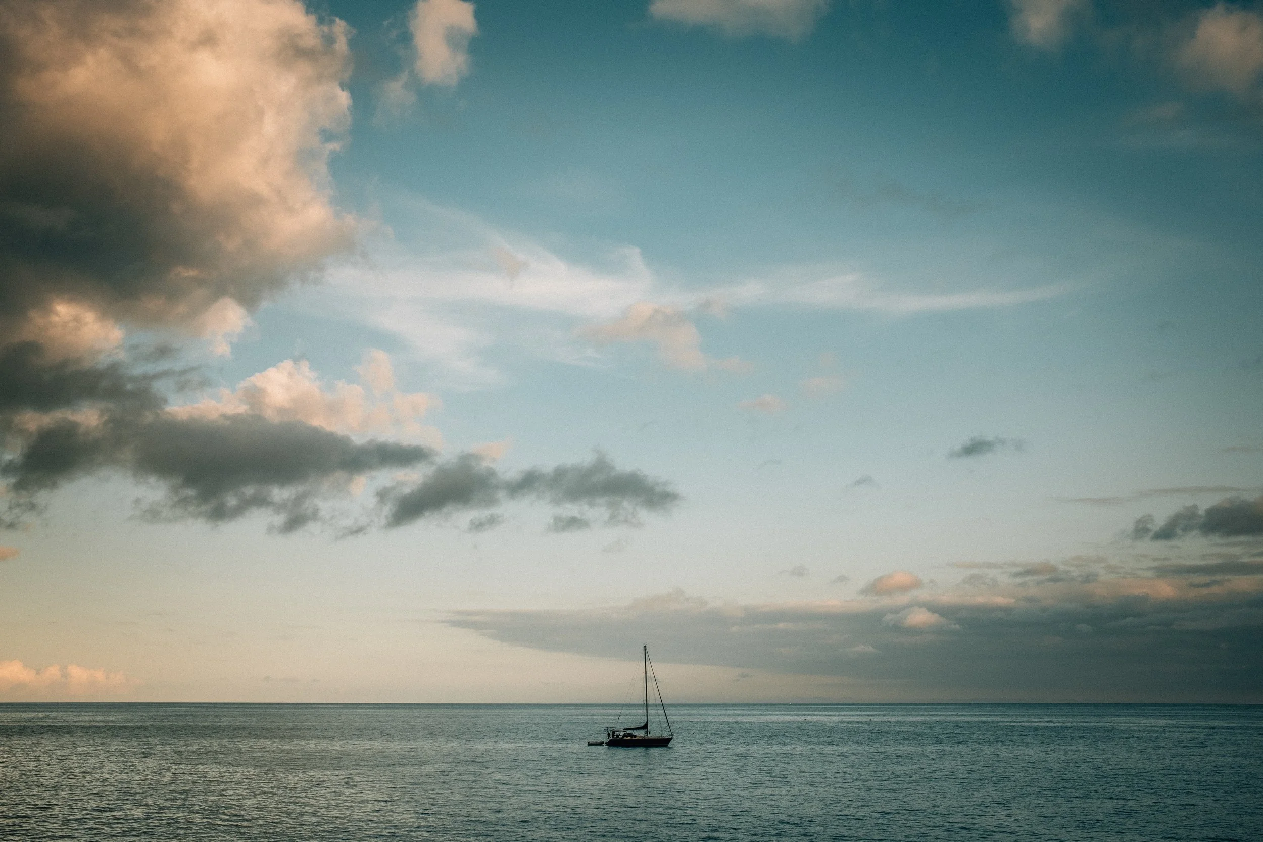 A sailboat on calm ocean waters under a partly cloudy sky during daytime.