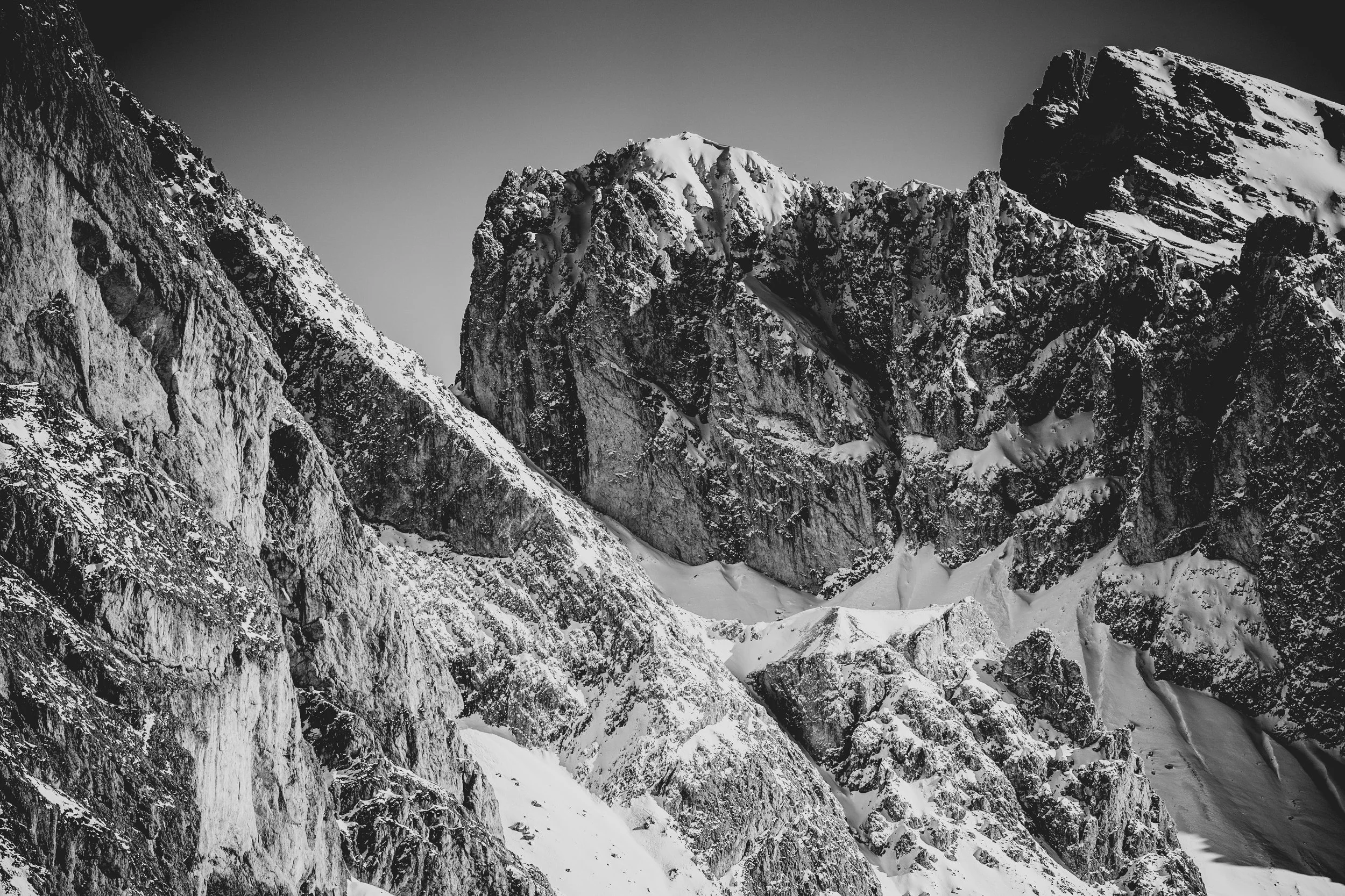 Black and white photo of snow-covered mountain peaks with steep cliffs and rugged terrain.