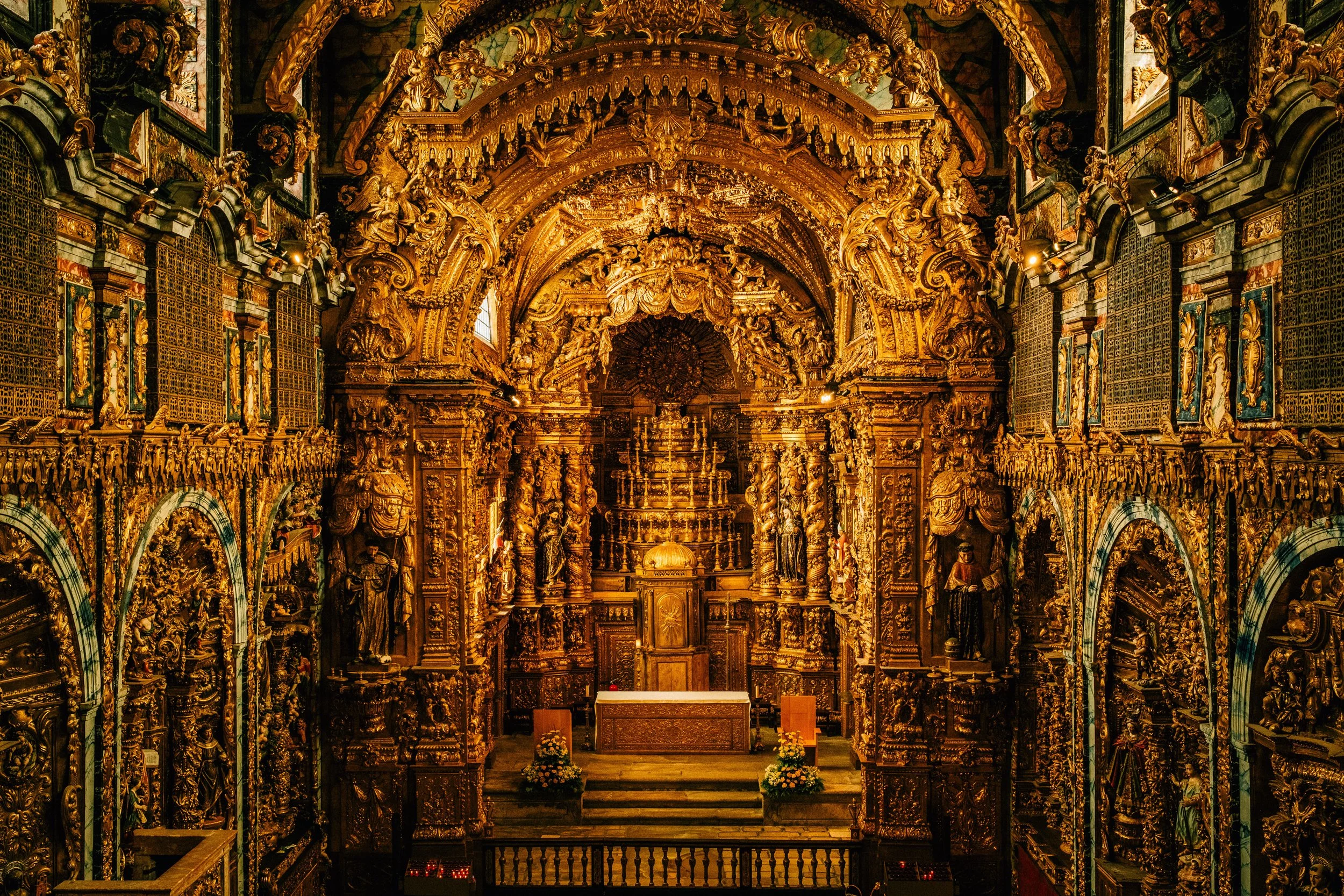 Interior of a richly decorated religious church or chapel with gold ornate carvings, statues, and religious icons, leading up to an altar.