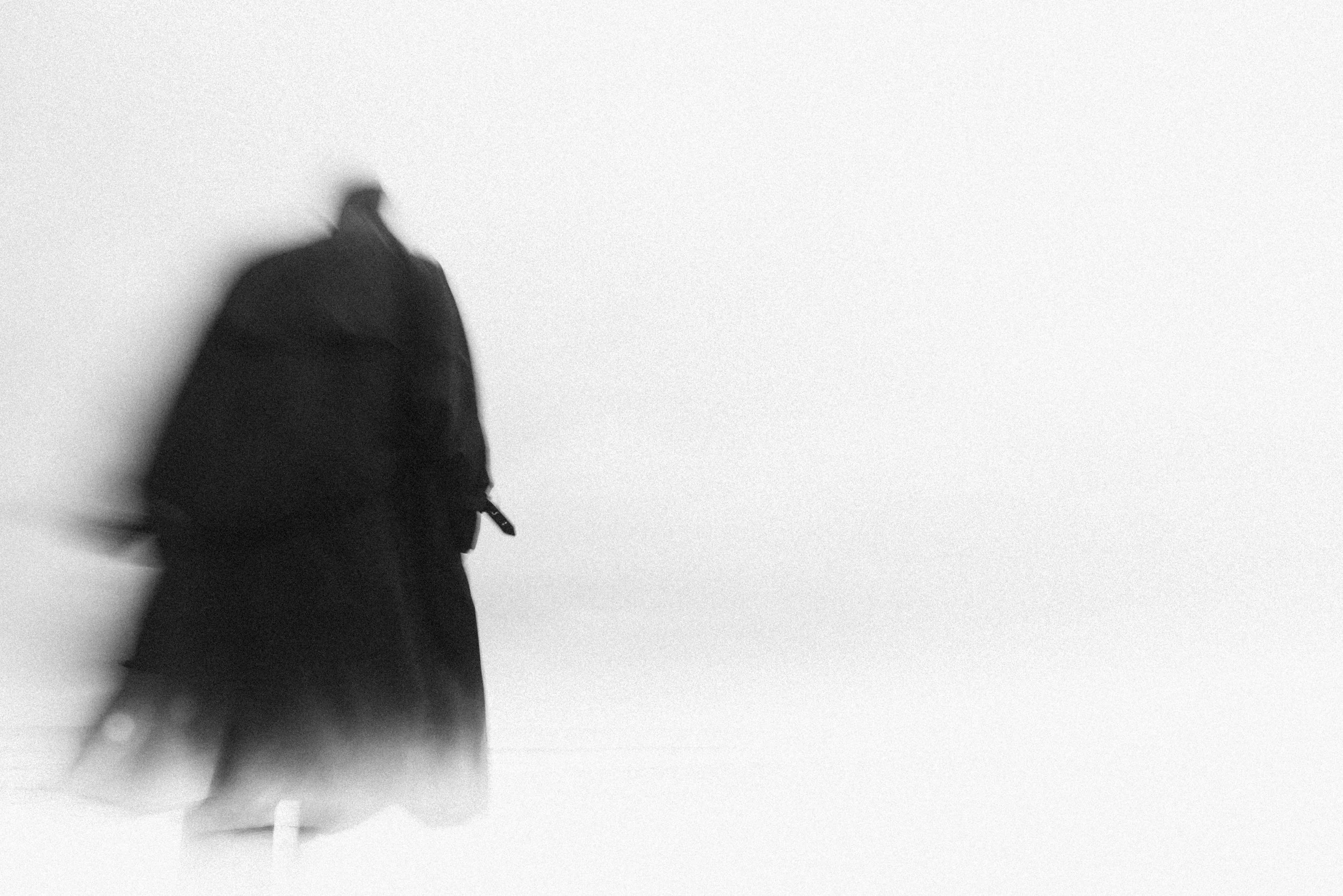 A blurry black jacket on a hanger against a plain white wall.