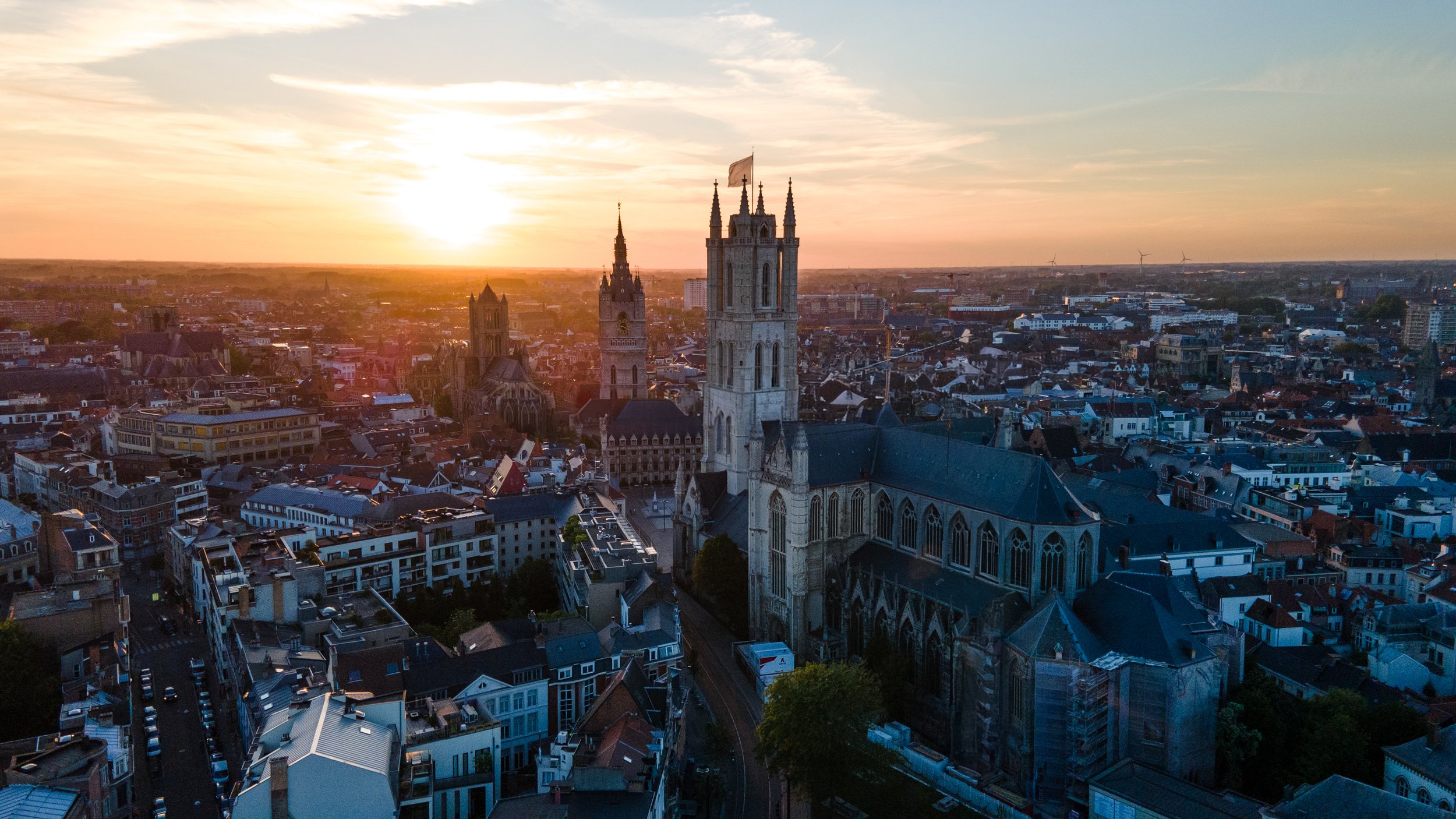 Cityscape at sunset showing a large church with tall towers and gothic architecture amidst residential and commercial buildings.