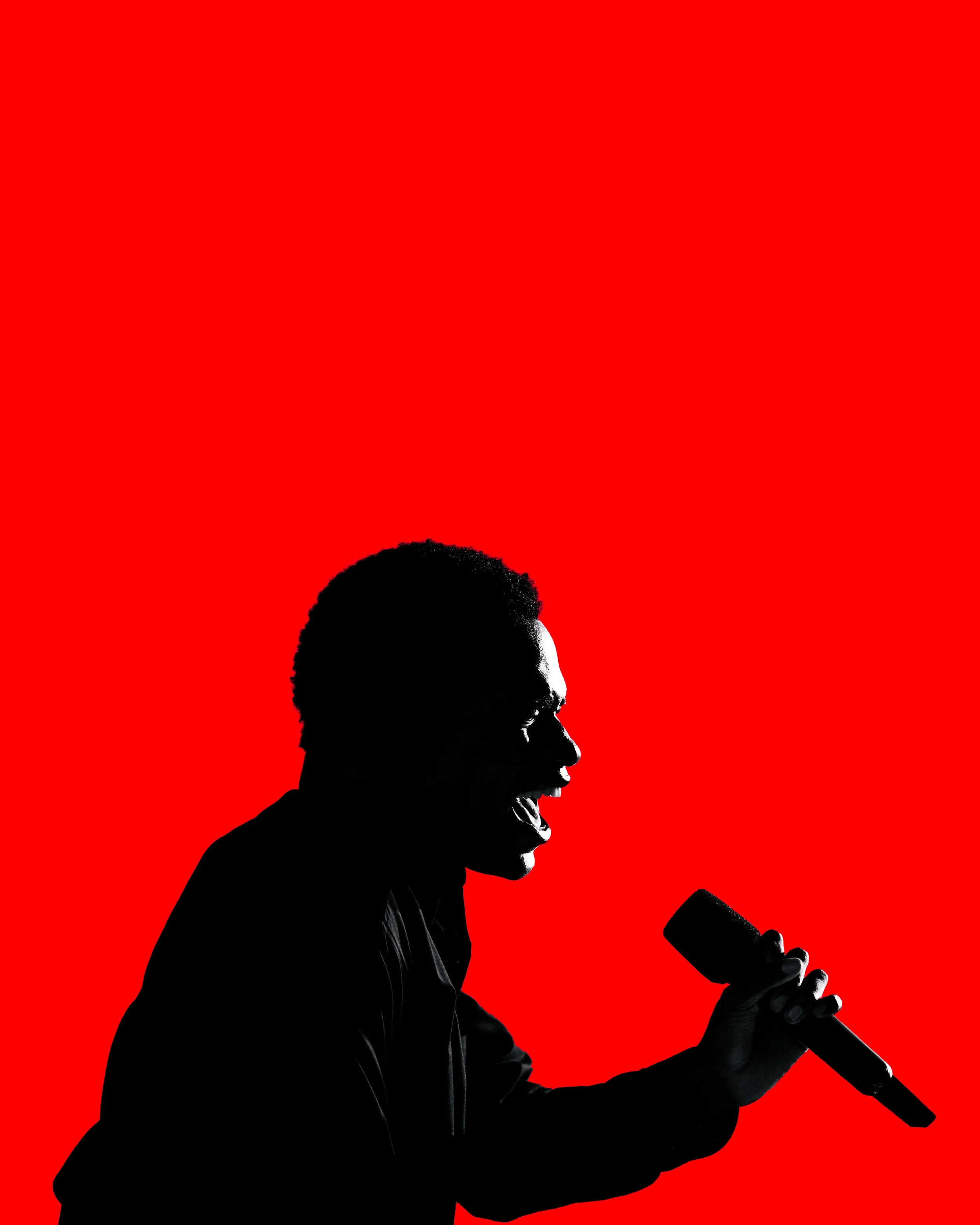 Silhouette of a young man holding a microphone and yelling against a red background.