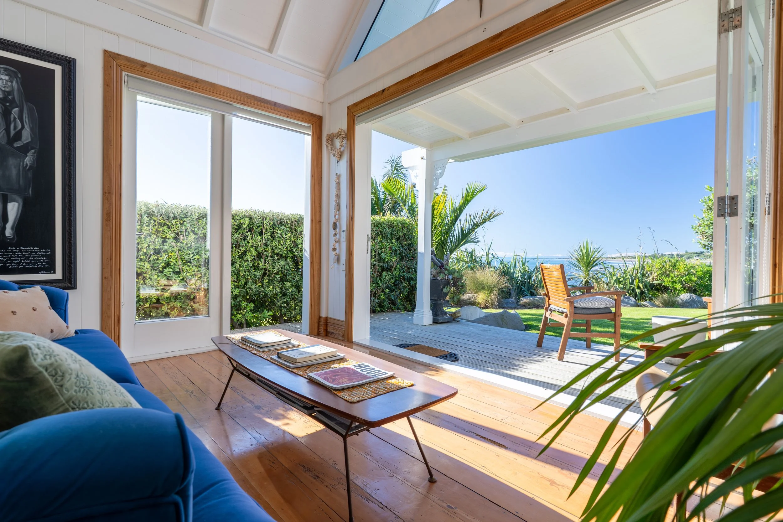 Room with large glass doors opening to a yard with palm trees and a view of the ocean on a sunny day.
