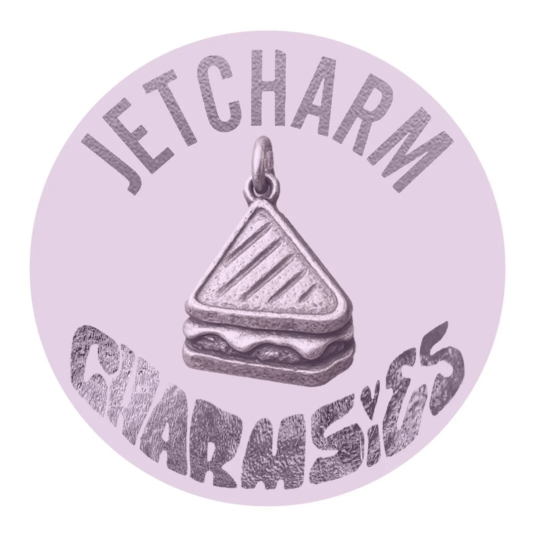 Jetcharm - A circular badge with a light purple background featuring a metallic sandwich charm in the center. The top arc of the badge reads 'JETCHARM' and the bottom arc reads 'CHARMS' in a textured font.