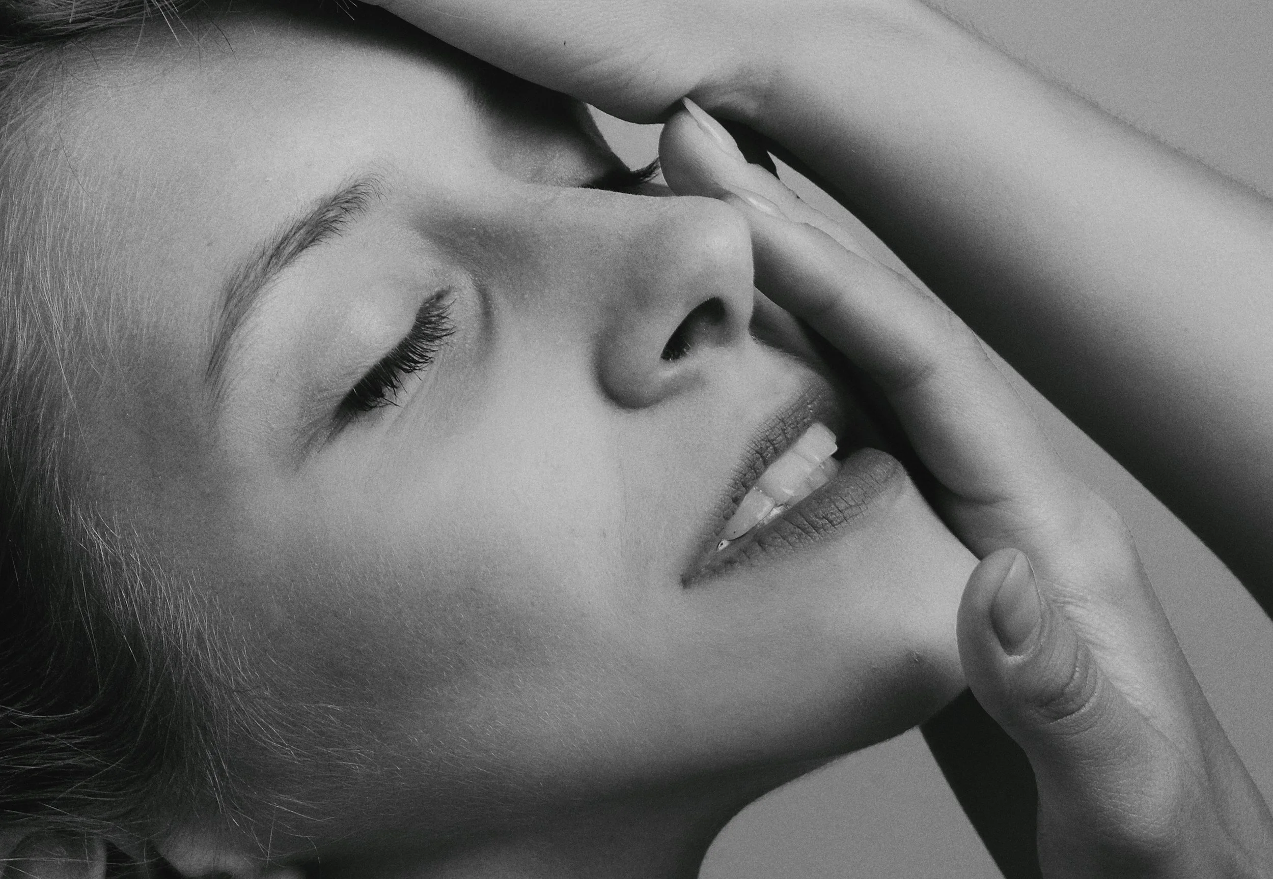 Woman touching her face, eyes closed, in a contemplative close-up portrait in black and white