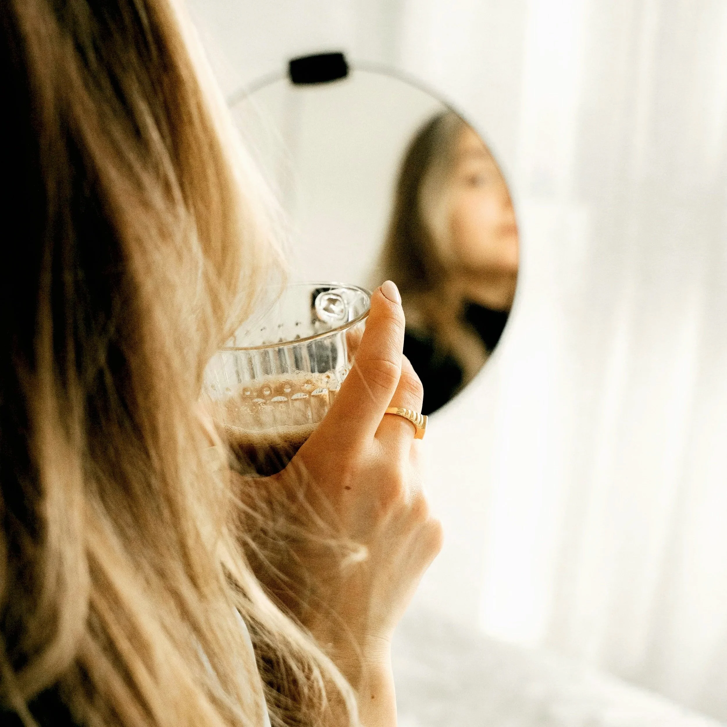 Woman looking in the mirror at the skin around her eyes in soft morning light