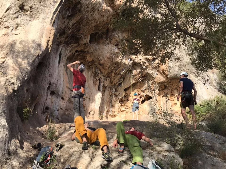 People rock climbing and resting on a rocky outdoor cliff with trees around.