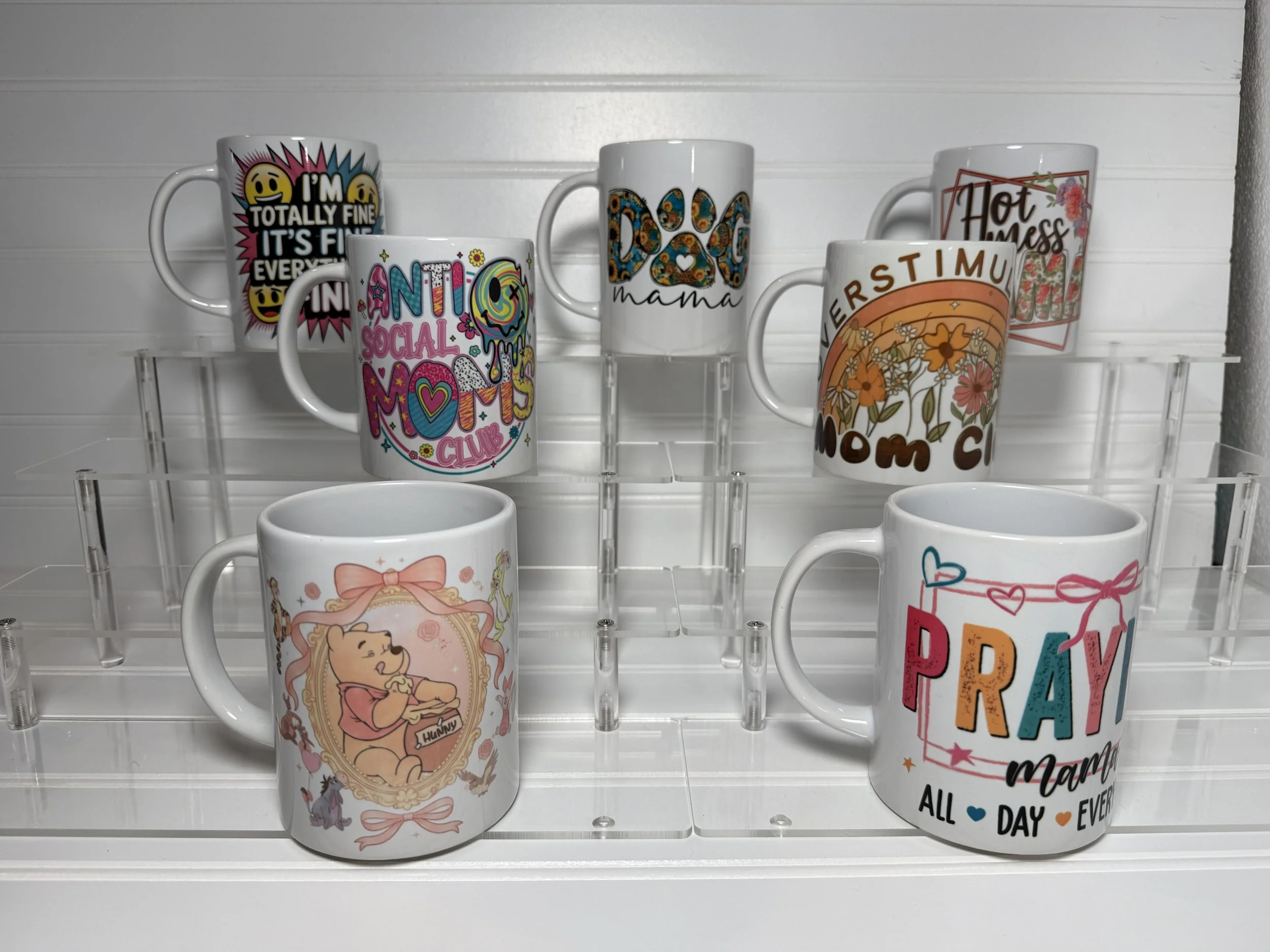 Collection of decorative mugs with colorful designs on a white shelf against a white wall.