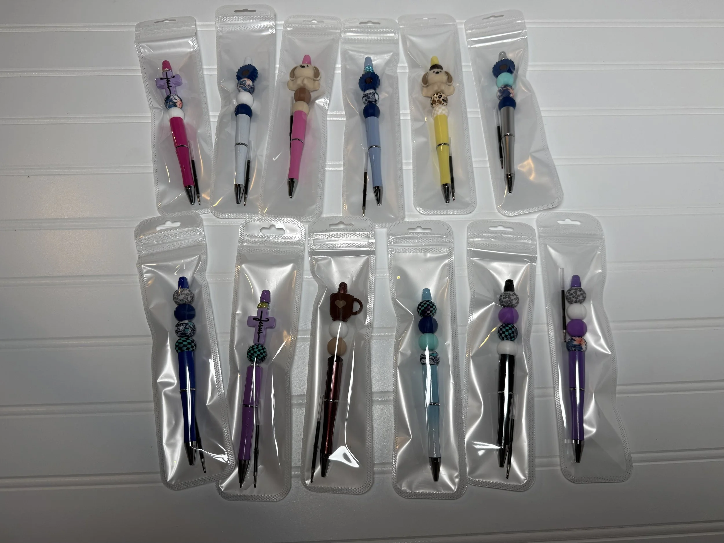 A collection of decorative pens in clear plastic packaging, featuring various colorful designs and character-themed toppers, laid out on a white surface.