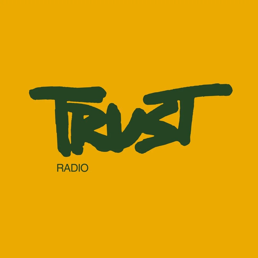 The image features a yellow background with the word "TRUST" written in large, green, graffiti-style letters. Below it, the word "RADIO" appears in smaller, plain black text.