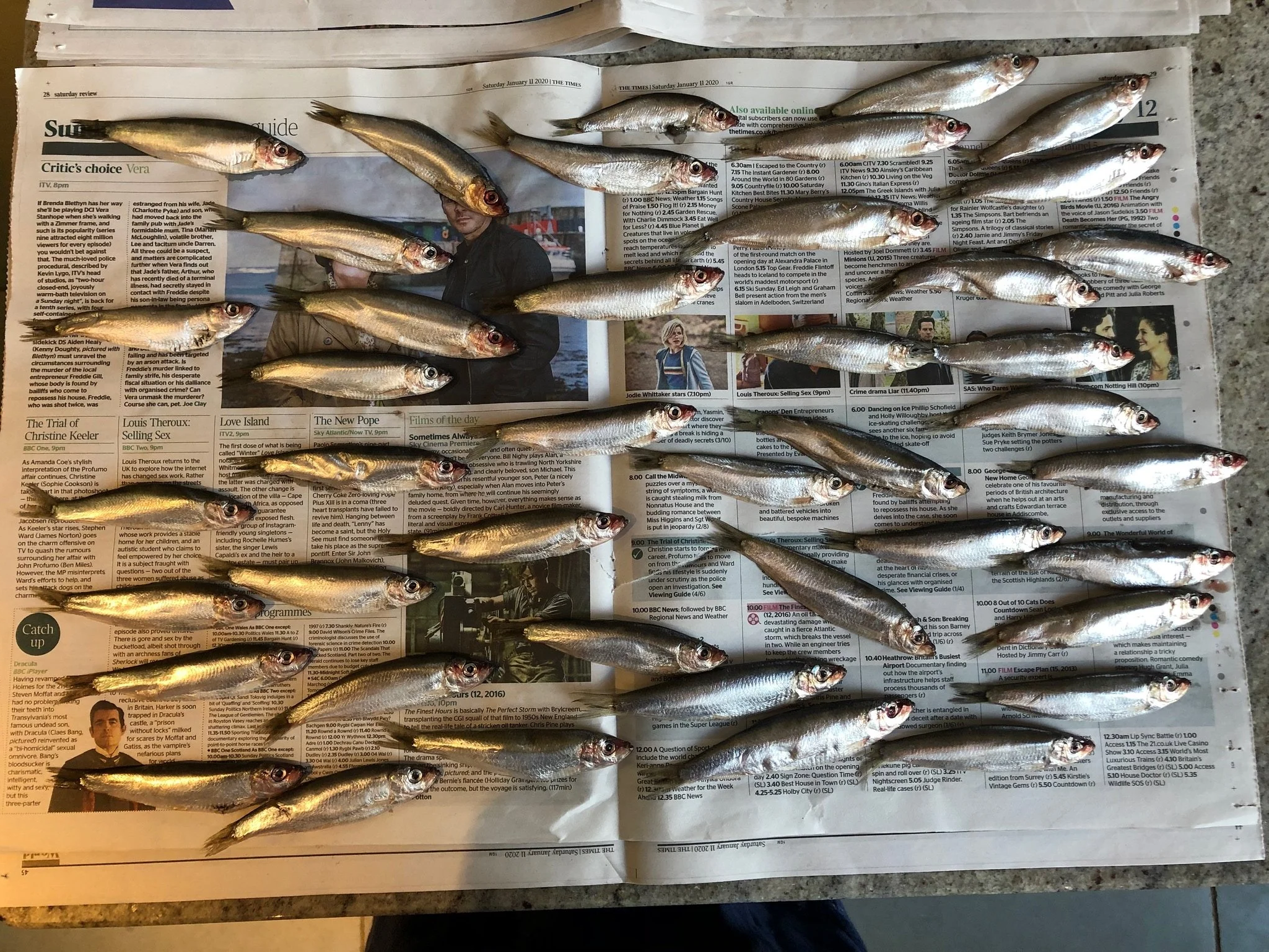 Multiple small fish placed on an open newspaper on a table.
