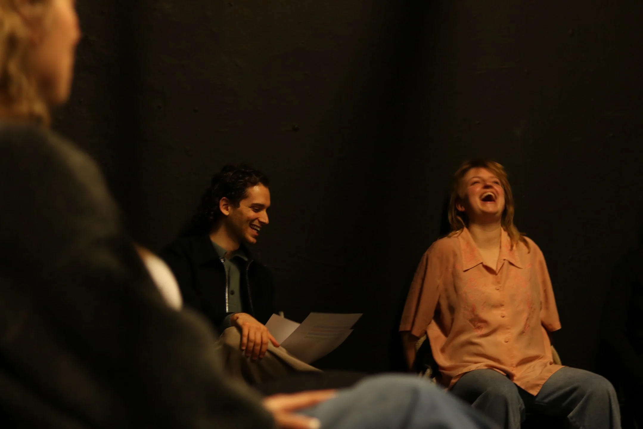 People sitting in a circle and laughing during a group discussion or meeting in a dark room.