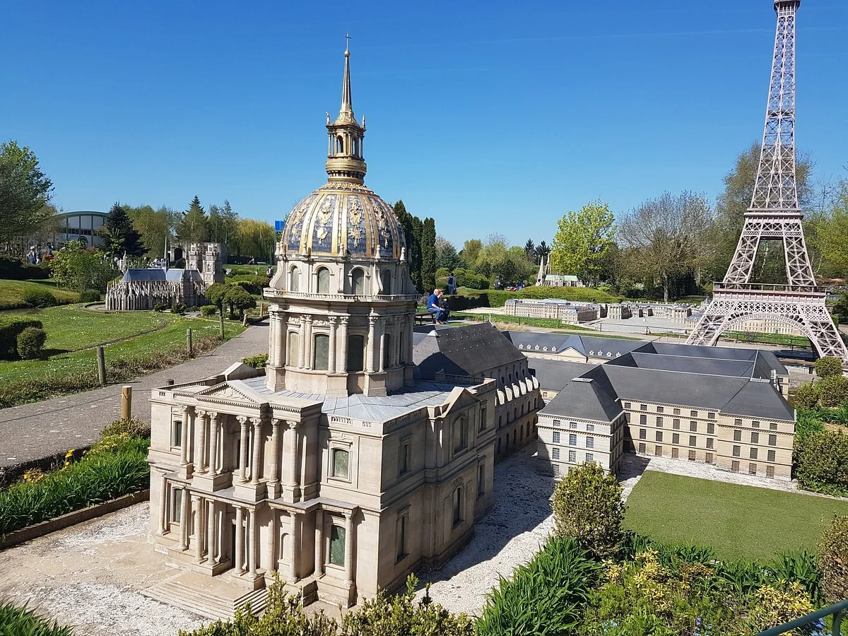 Miniature replicas of Paris landmarks, including Sacré-Cœur Basilica and Eiffel Tower, in a park setting with trees and pathways