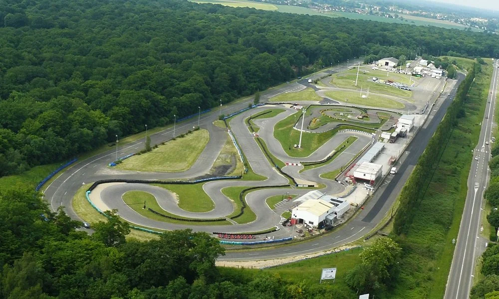 An aerial view of a go-kart race track surrounded by trees and located next to a highway.