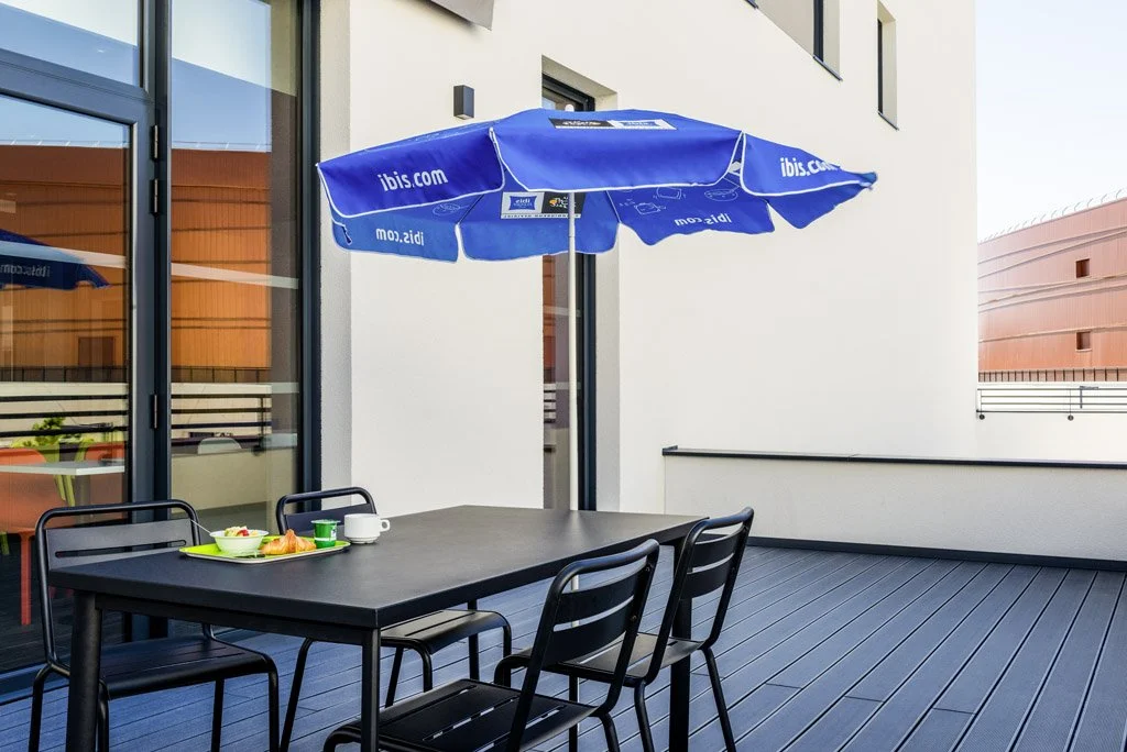 Balcon avec une table, des chaises, un parasol bleu, et un petit déjeuner