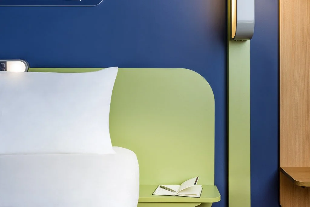 Coin lecture avec un livre ouvert posé sur une table à côté d'un lit avec une tête de lit vert clair et un mur bleu.