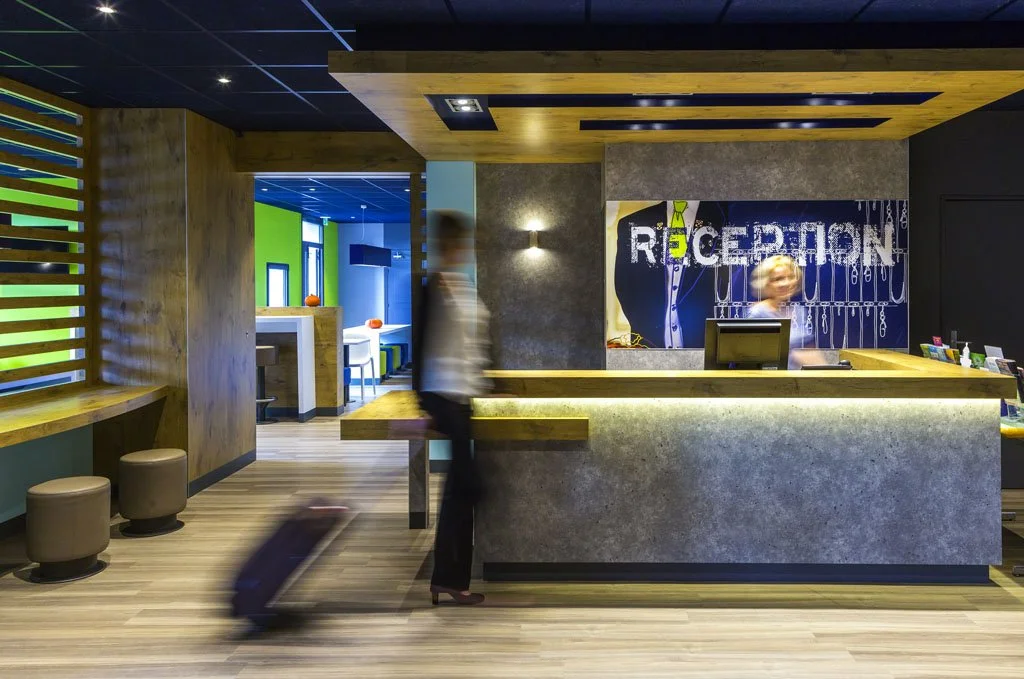 Intérieur moderne à la réception d'un hôtel ou centre de services, avec un comptoir en béton, une réceptionniste et un client avec une valise.