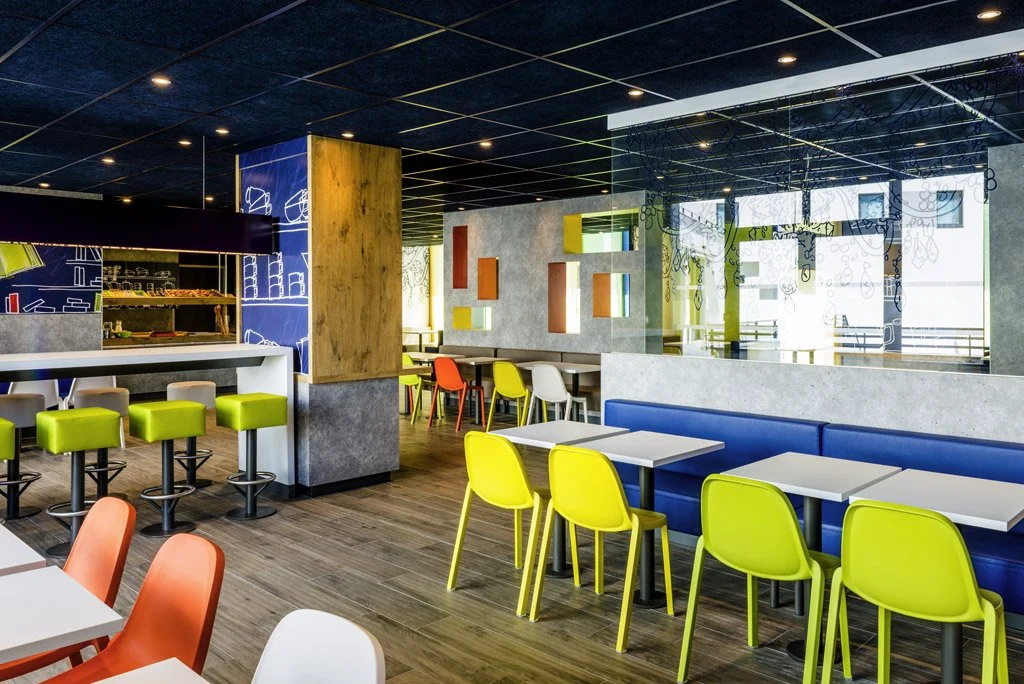 Salle de café ou restaurant moderne avec des tables, des chaises colorées, un comptoir et une décoration contemporaine.