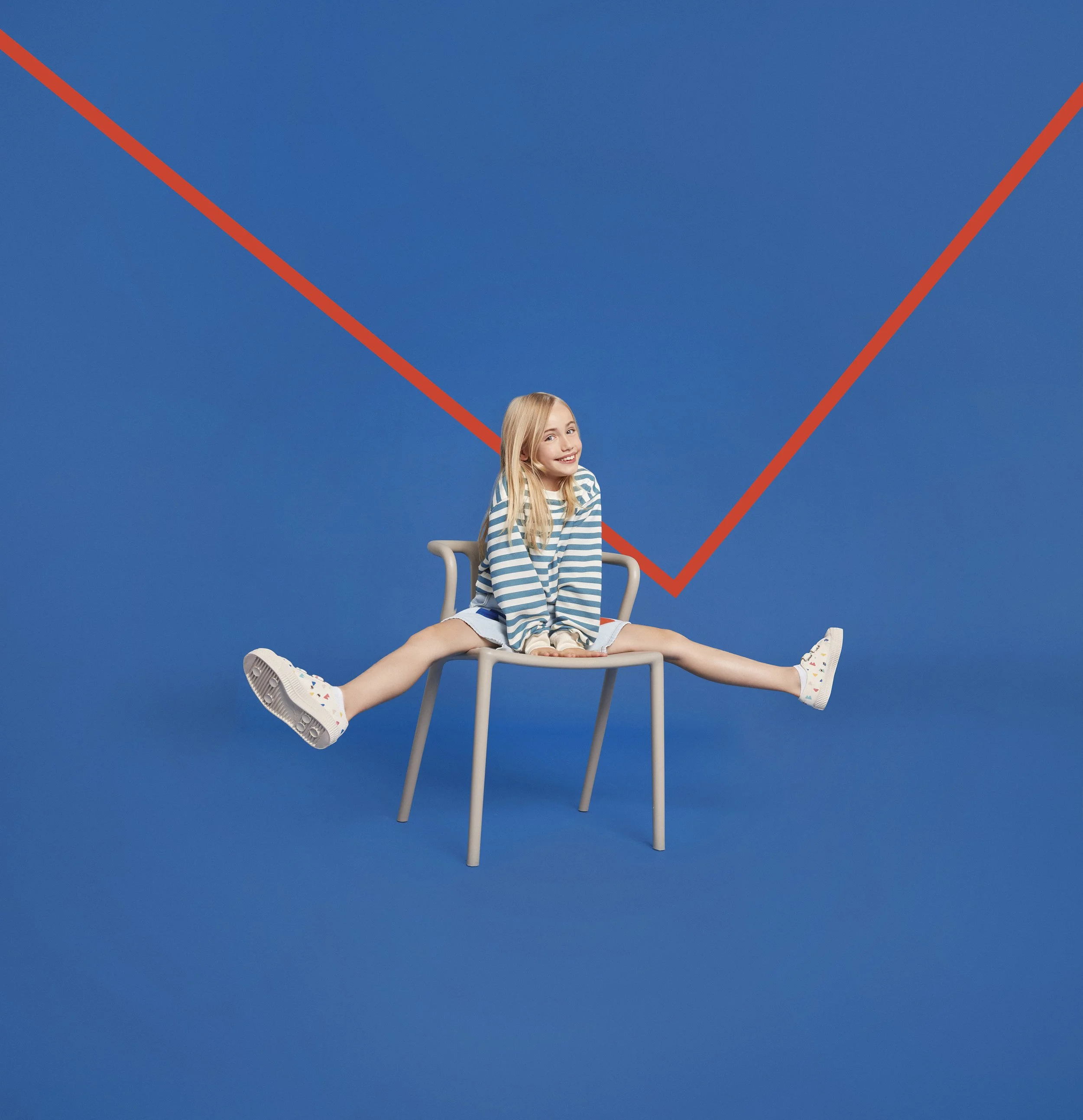 Une femme assise sur une chaise, esquissant un sourire, avec un fond bleu. La photo est teintée de bleu et met en avant la femme et la chaise, avec un décor minimaliste.