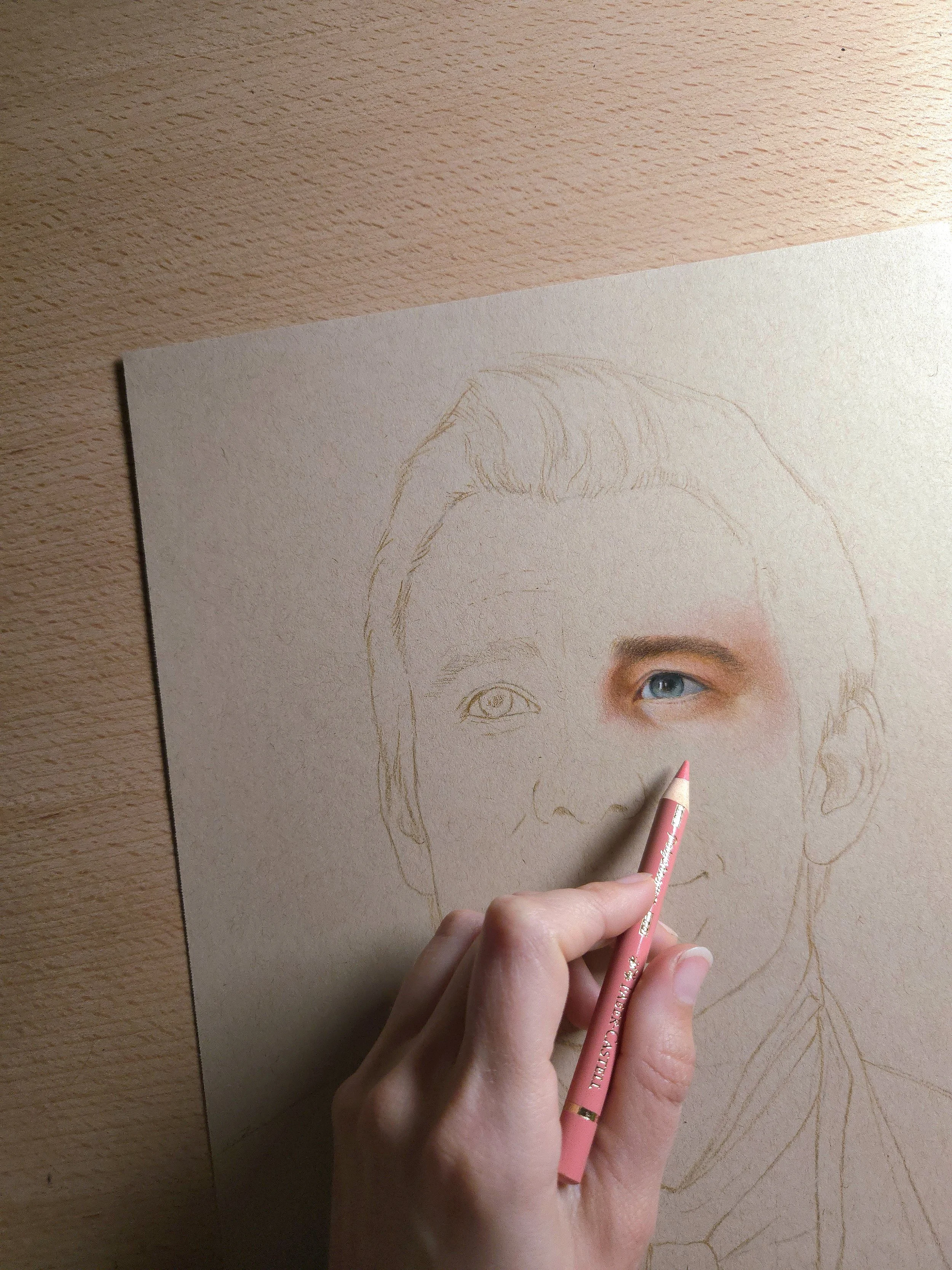 A person is drawing a realistic colored portrait of a woman with blue eyes on a piece of paper using colored pencils.