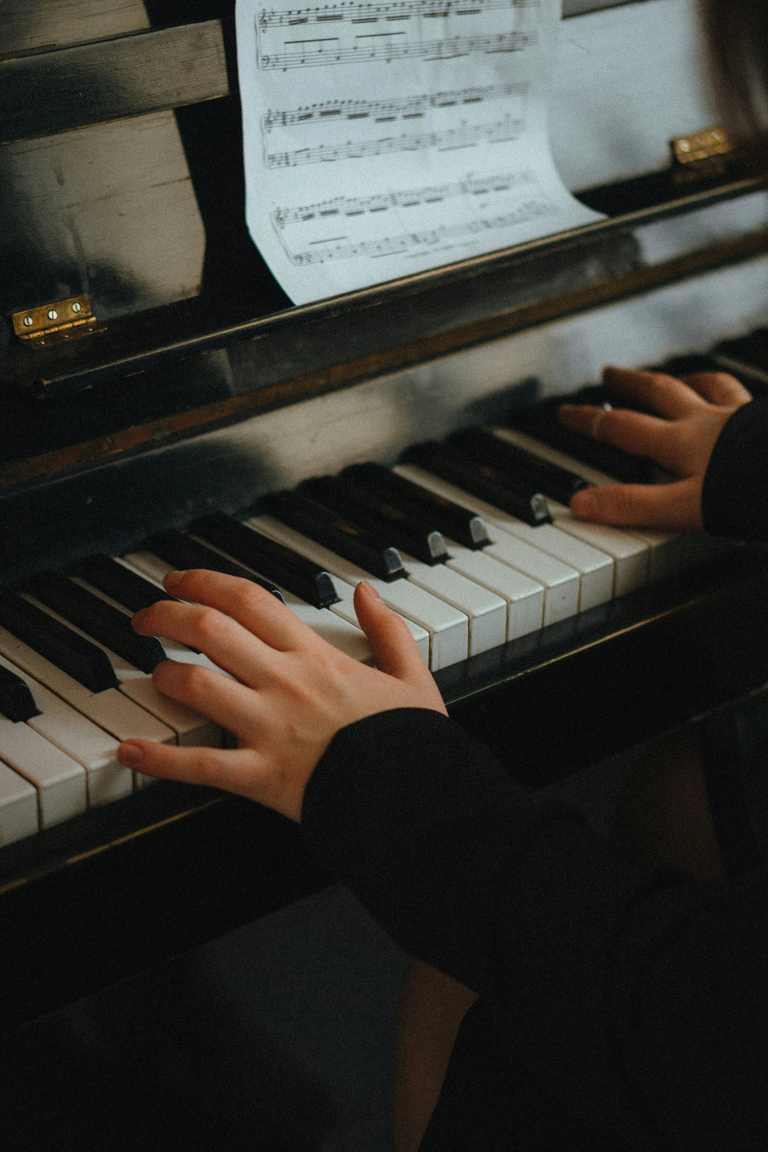 Hands playing piano with sheet music on a music stand.