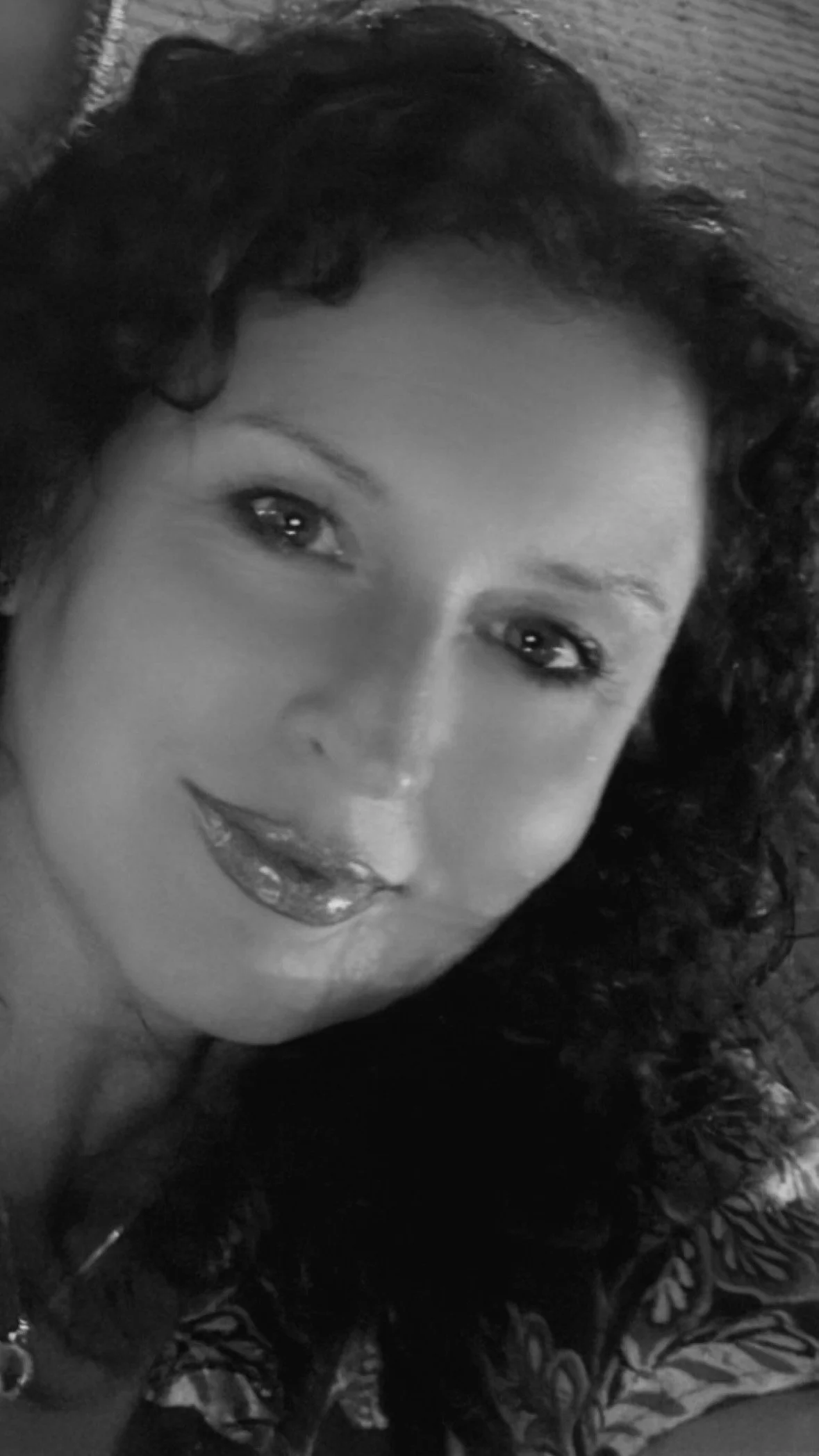 Close-up of a smiling woman with dark, curly hair, wearing a patterned garment, in black and white.