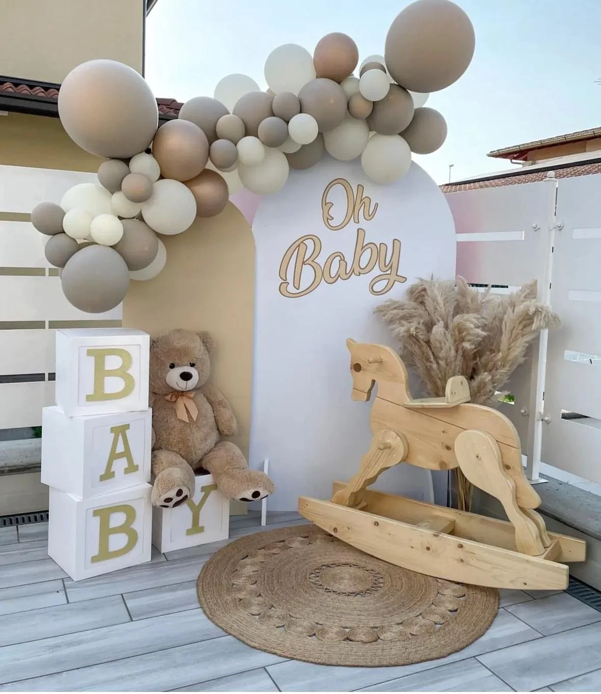 Decorazioni per una festa di benvenuto al neonato con palloncini, cubi con lettere, orsacchiotto, cavallo a dondolo in legno e fiori di pampas.