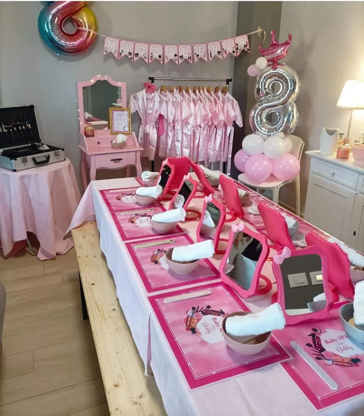 Festa di bambina con decorazioni rosa, balocchi, vestiti rosa e tavolo apparecchiato con specchietti e tazze