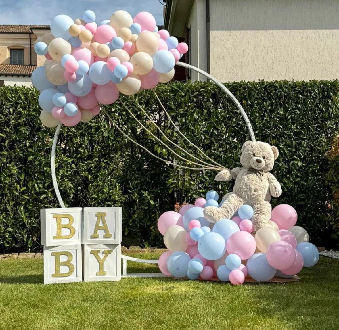 Decorazione di modo con un orsacchiotto di peluche, palloncini rosa, azzurri e beige, e blocchi con le lettere B A B Y.