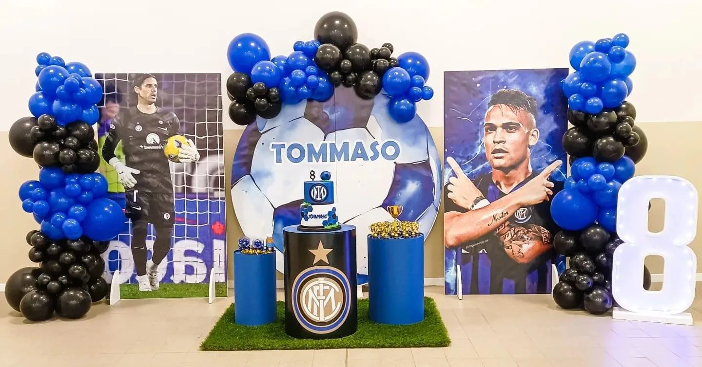 Decorazione di festa su tema calcio con immagini di due calciatori, palloni, e il nome Tommaso, con bottiglie di medaglie e un grande numero otto, decorazioni blu e nere.
