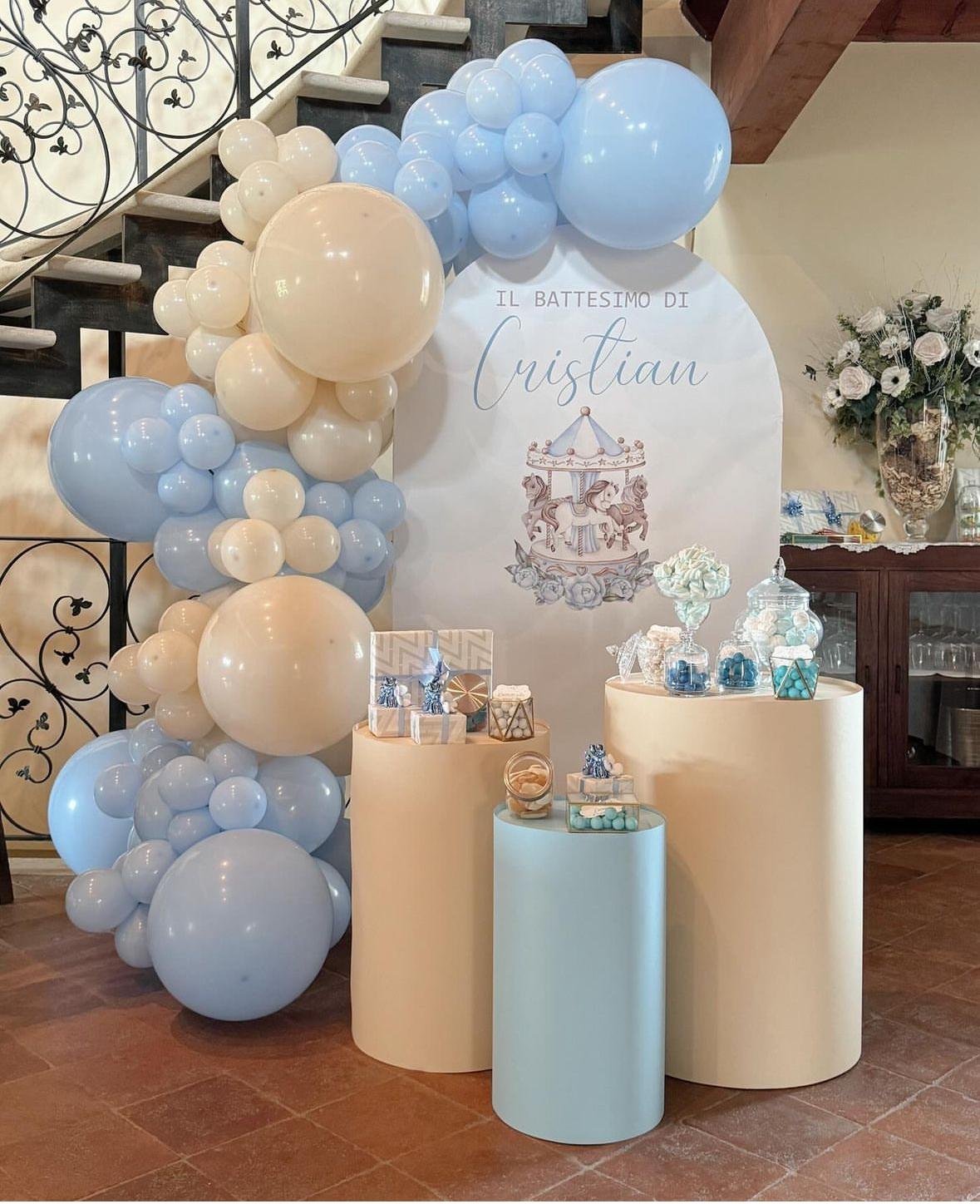 Decorazioni per il battesimo di Cristian, con palloncini azzurri e creme, un fondale con scritto 'Il Battesimo di Cristian' e una vasca carousel con cavalli, insieme a un tavolo ricco di confetti e regali.