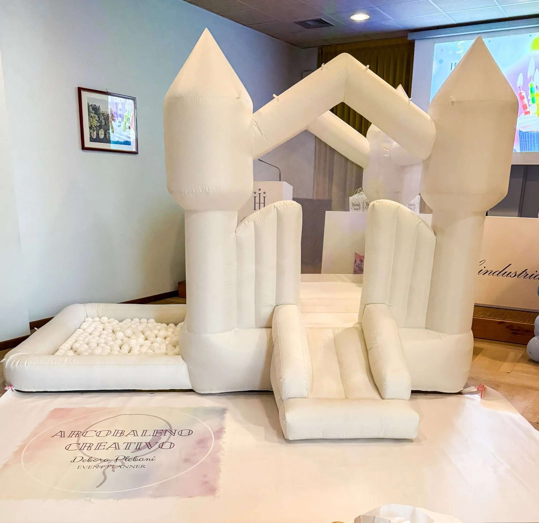 Castello gonfiabile bianco con torre e ponte, decorato con palline bianche, usato come attrazione per bambini in un evento.