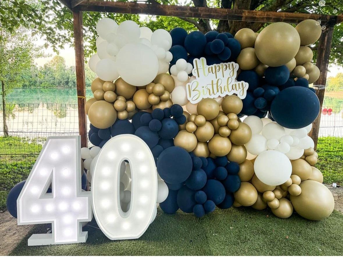 Decorazione di compleanno con palloncini bianchi, dorati e blu, una scritta 'Happy Birthday' e un numero 40 luminoso.