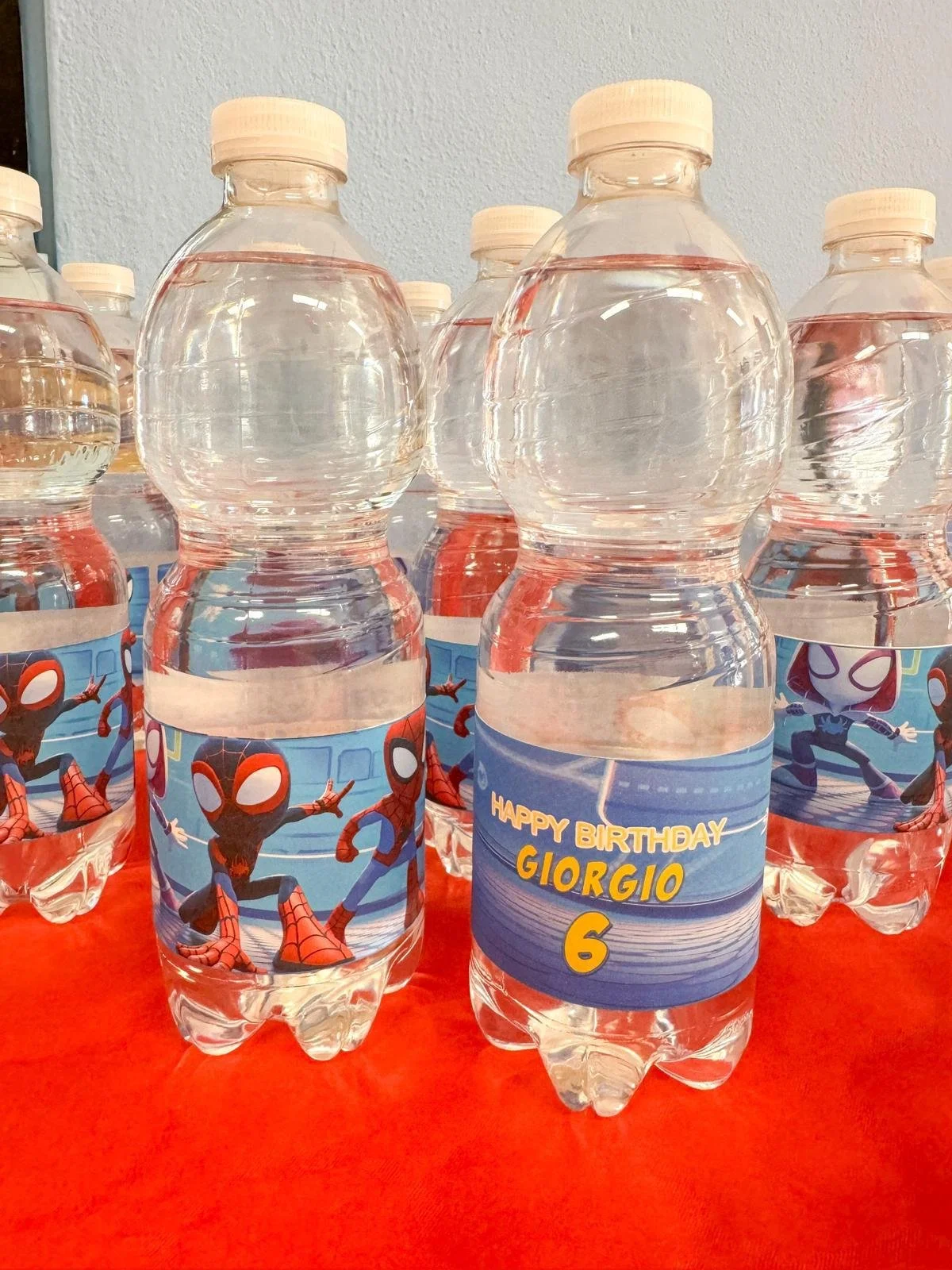 Bottiglie d'acqua con etichette di Spider-Man e un cartello di compleanno in italiano