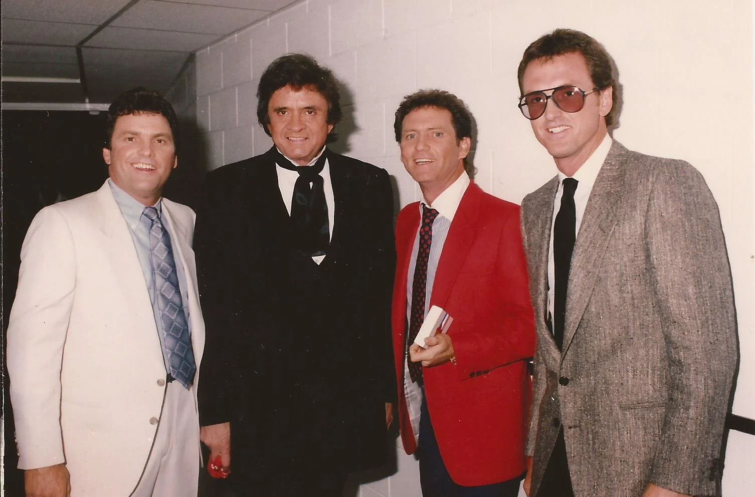 Group of four men, including Larry Gatlin and Johnny Cash, dressed in vintage formal attire, standing together in a hallway.
