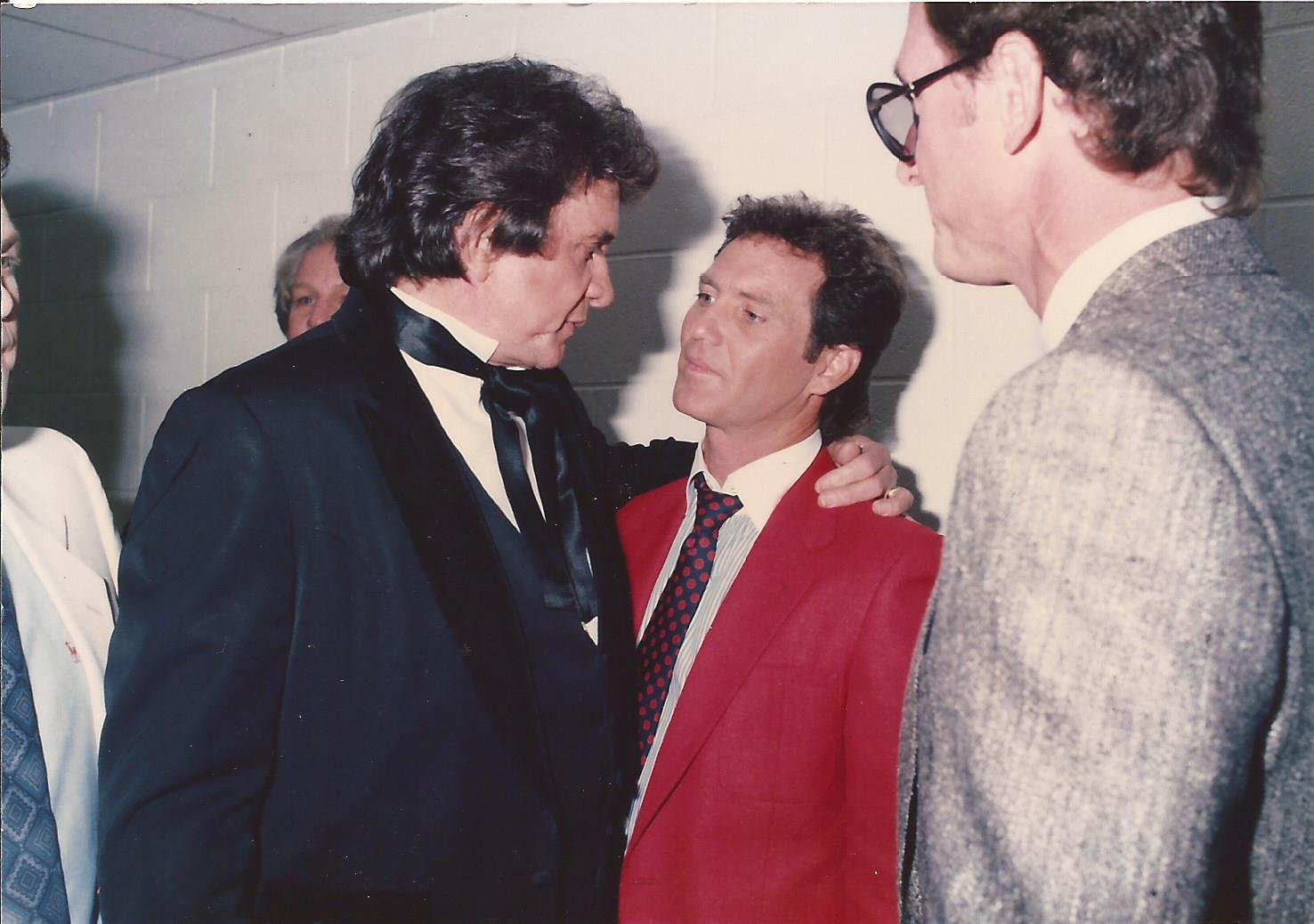 Four men in suits, engaged in intense conversation in a hallway, with one man placing his hand on another's shoulder.