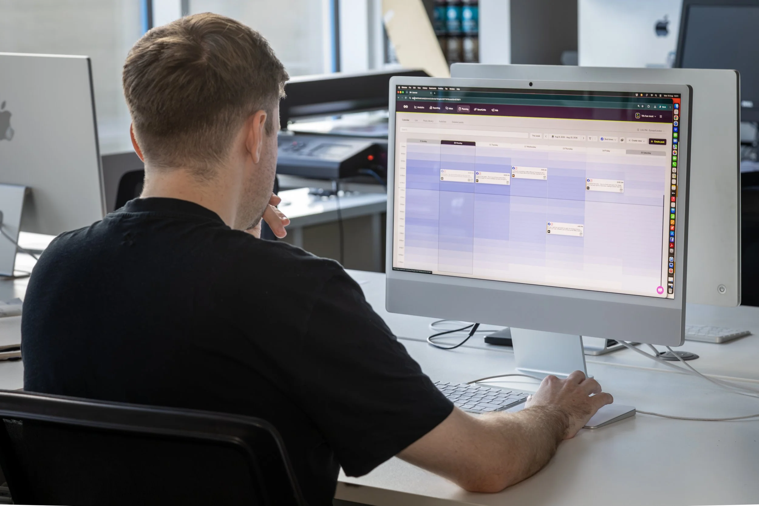 A man sitting at a white desk working on a computer in an office environment.