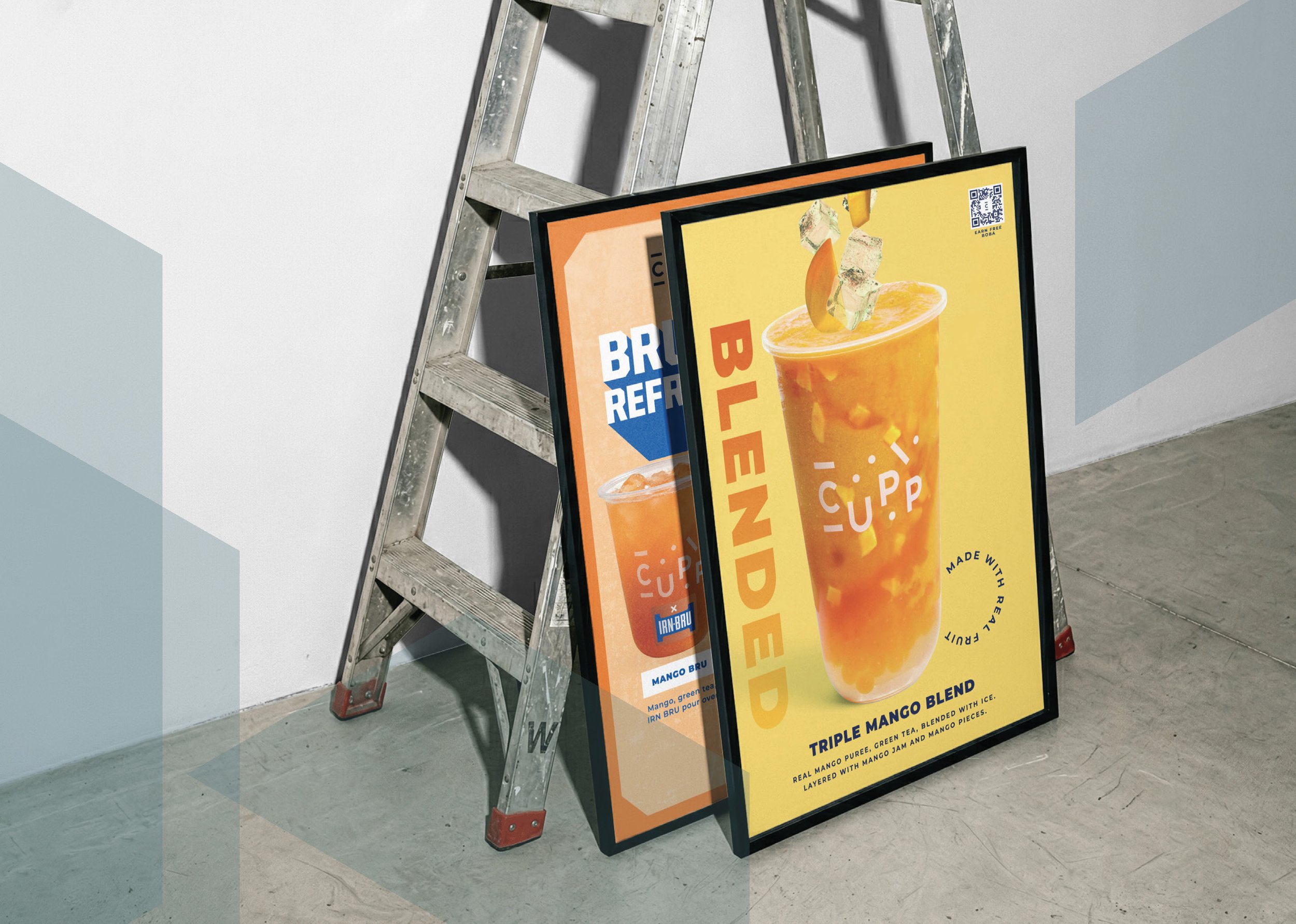 A large, colorful advertisement sign by Yellow Slate Design. For a CUPP mango smoothie layered with mango jam and pieces, lying against another for an IRN BRU boba tea, placed against a wall with a ladder next to it.