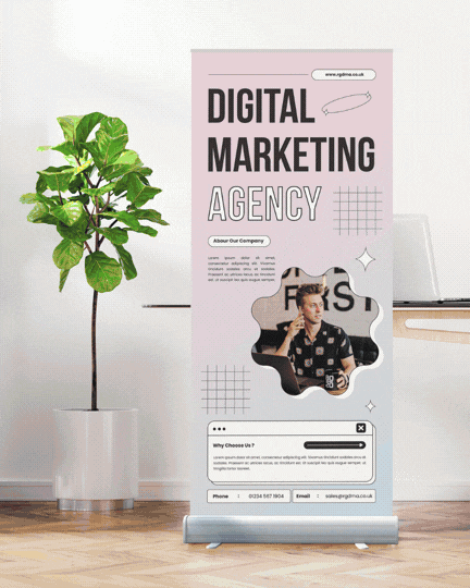 A promotional standee for a digital marketing agency featuring a photo of a young man in a patterned shirt, a potted plant, and a laptop on a white desk.