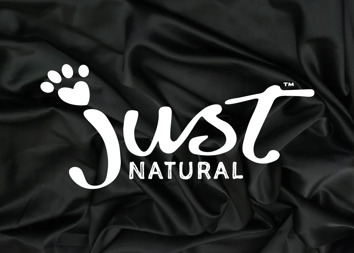 White text overlay reading "Just Natural" with a paw print and heart design on a dark, crinkled fabric background.