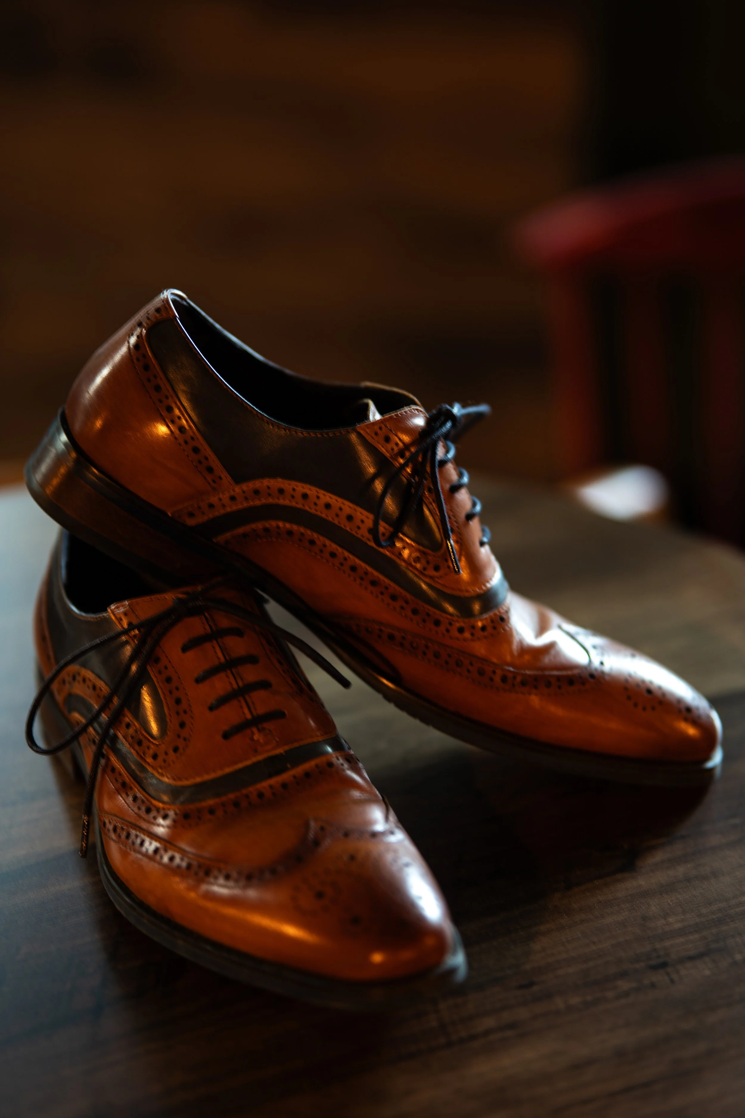 A pair of vintage leather dress shoes with brown and black color, placed on a wooden floor.