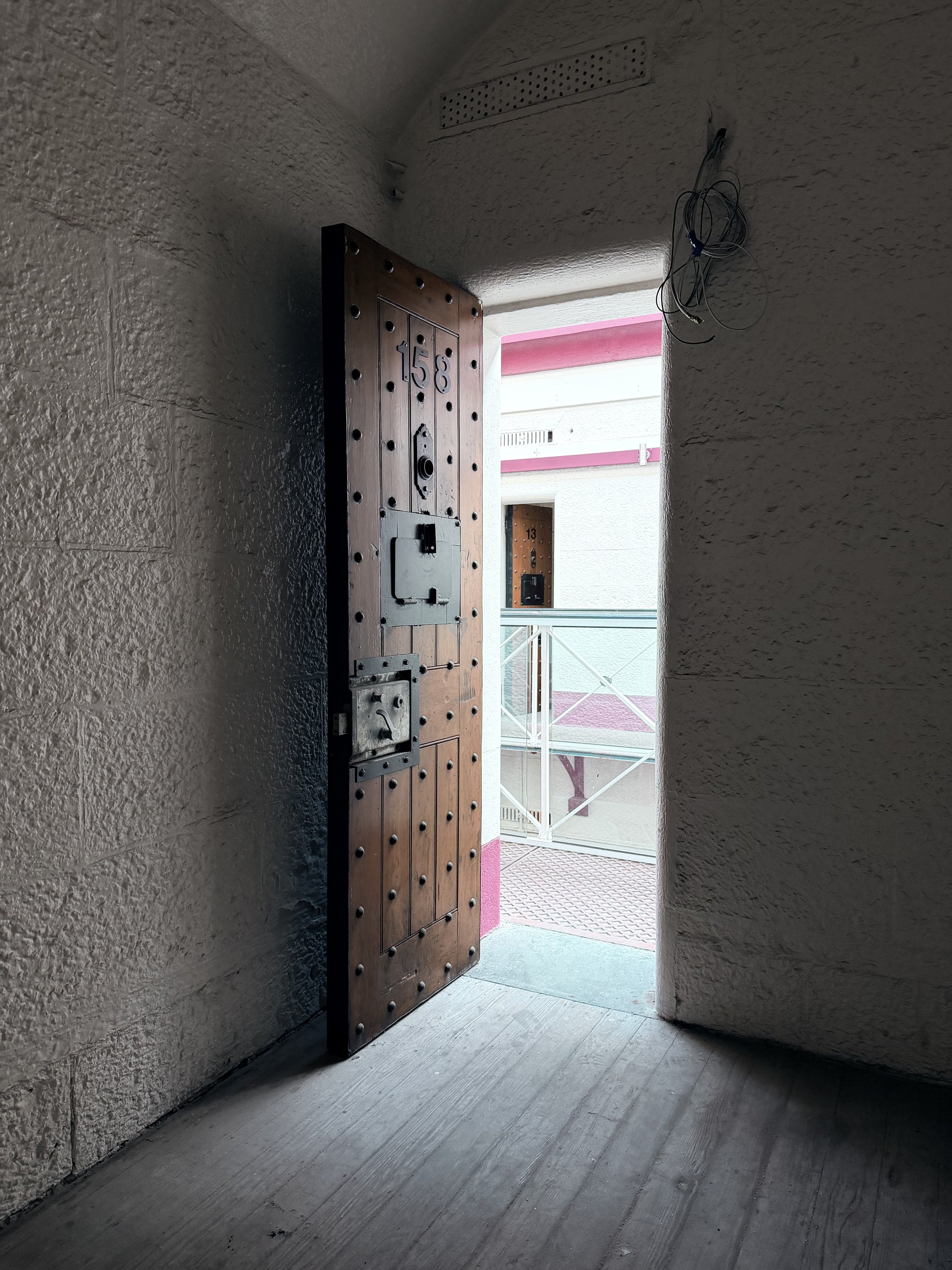 Open wooden door leading to an outdoor balcony with white railings and a pink and white building in the background.