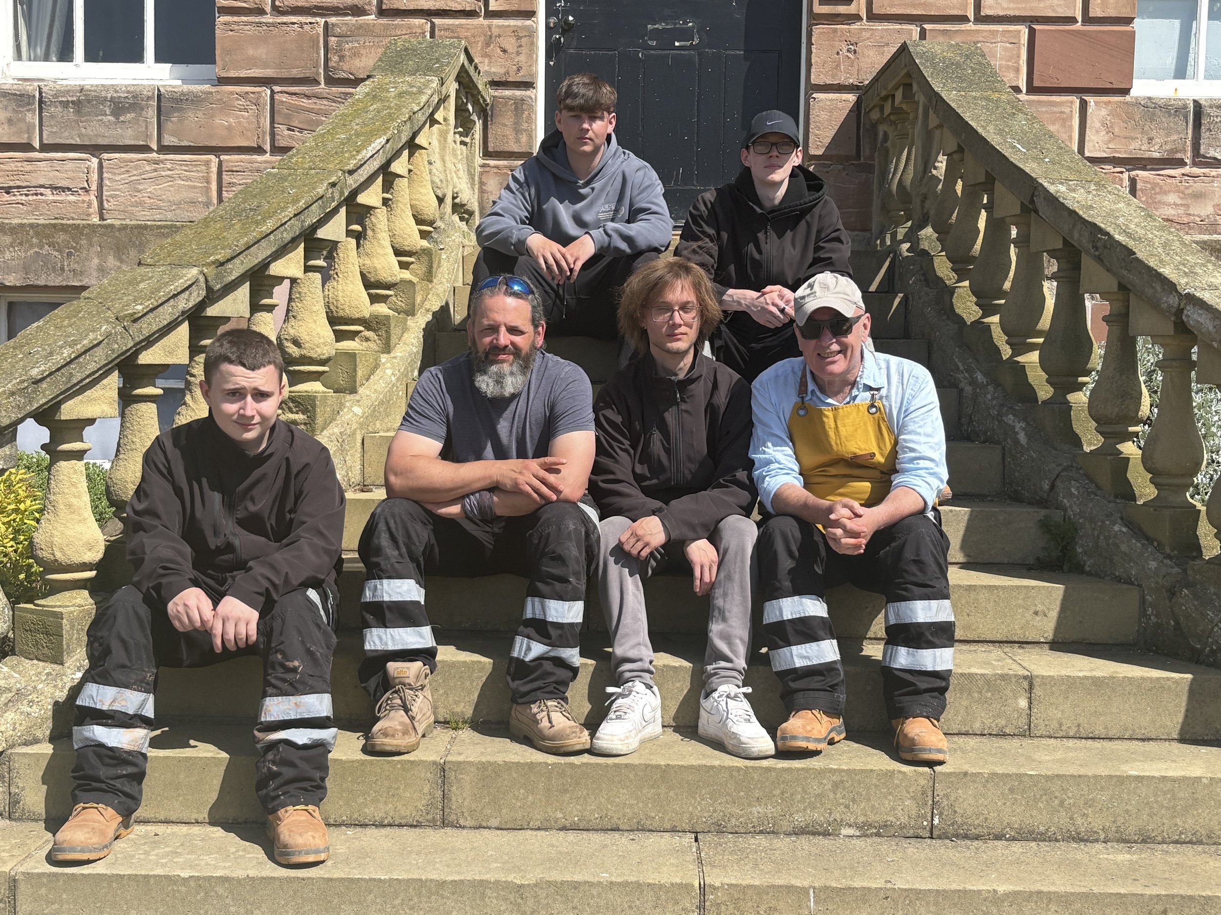 group of men in working clothing sitting on stone steps