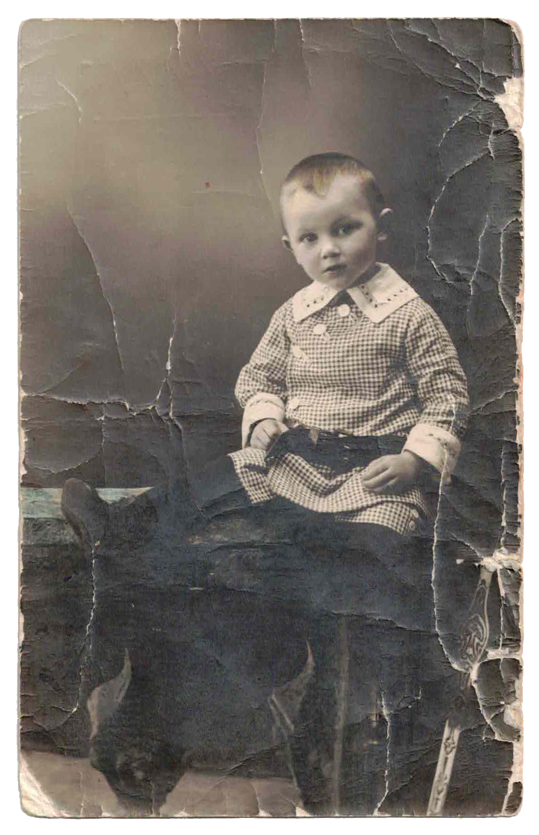Black and white photo of a young boy sitting on a chair with a torn and worn background.