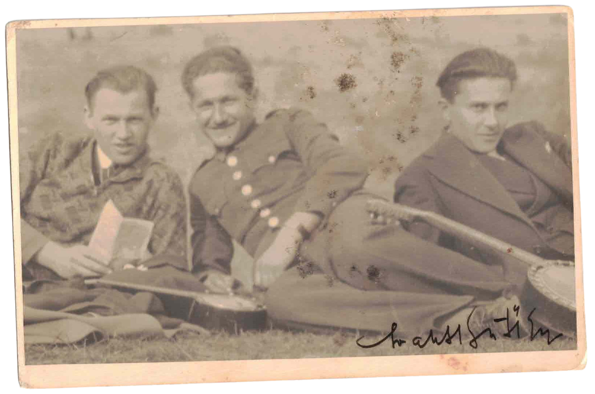 Three young men in military uniforms sitting on the ground, holding musical instruments, with one holding a book, in front of a textured background, with an illegible signature at the bottom right.
