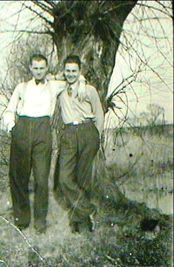 Two young men standing next to a large tree outdoors.