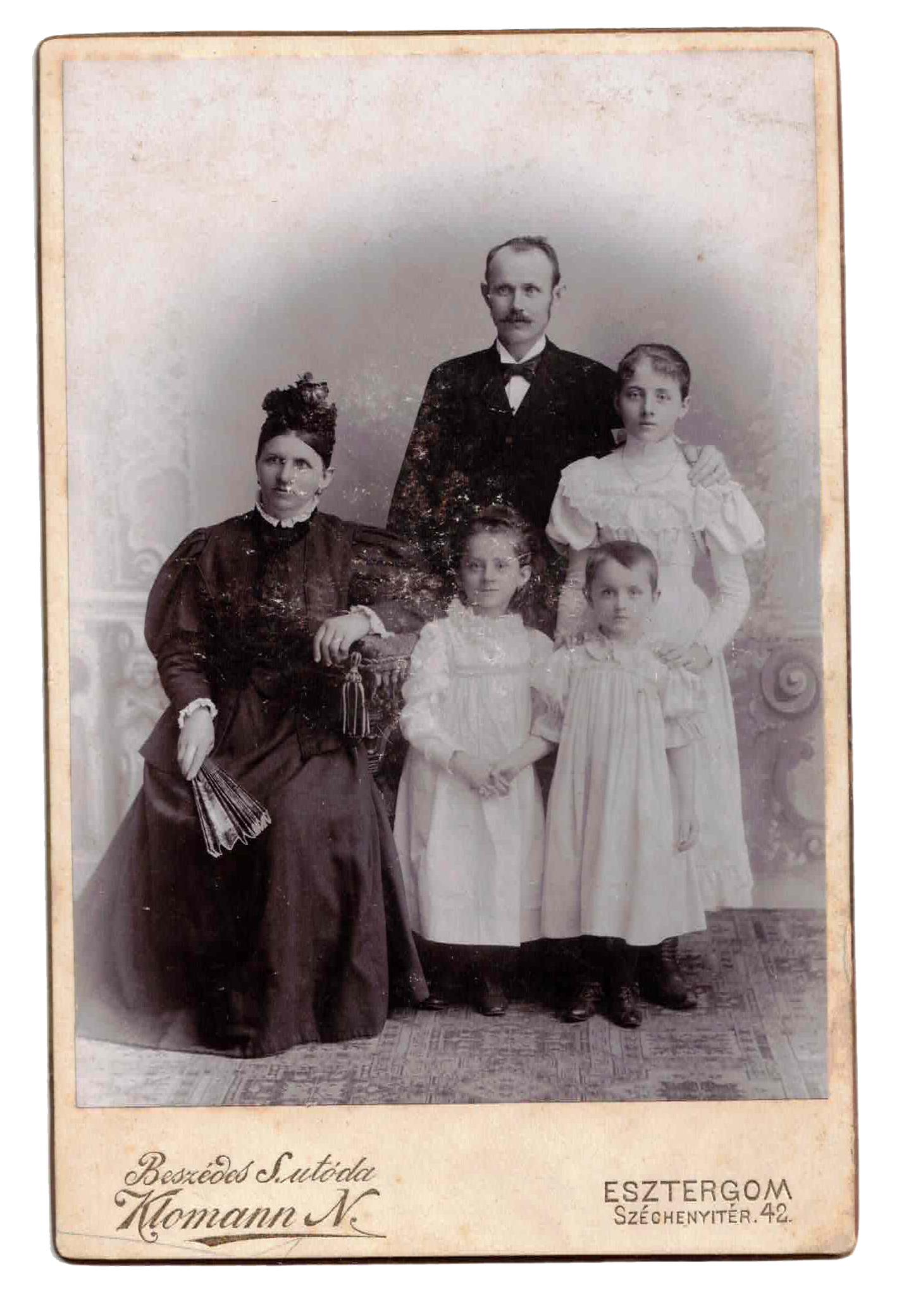 Black and white vintage photograph of a man with three children in formal attire, with two children standing and one sitting, possibly from the late 19th or early 20th century, with handwritten text below.