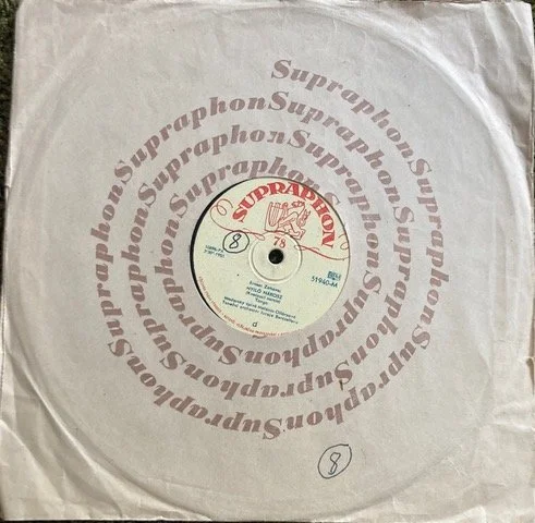 A vinyl record partially inside a paper sleeve, with a red 'SUPRAPHON' sticker on its label, and the pattern 'SupraPhon' repeated in a circular layout on the sleeve.