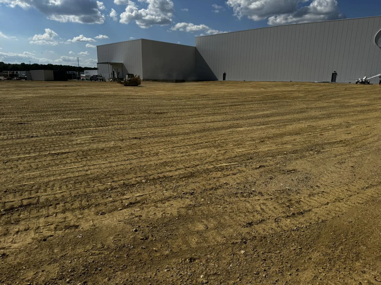 Large industrial building under construction with a dirt lot in the foreground and construction equipment nearby.